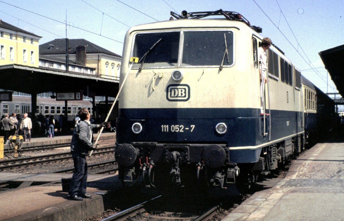 111 052-7 in Regensburg am 15.05.1982. Es wird für gute Sicht gesorgt. Heute sieht man solche Aktionen aufgrund Insektenrückgangs kaum noch.