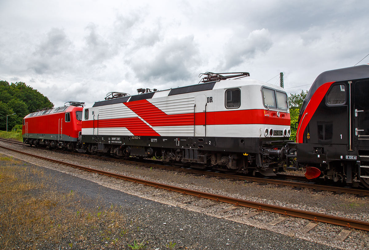 Am 05.07.2021 in Scheuerfeld (Sieg) beim Kleinbahnhof der WEBA (Westerwaldbahn) stehen bereit für ihre nächste Aufgabe, der Abfuhr von schweren Holzzügen: 
In der Mitte die  “Weiße Lady” 143 822-5, alias 243 822-491 80 6143 822-5 D-EBS der EBS - Erfurter Bahnservice GmbH, ex RBH 139, ex DB 143 822-5. ex DR 243 822-4.
Links die 156 002-8 (91 80 6156 002-8 D-FWK) der FWK - Fahrzeugwerk Karsdorf GmbH & Co. KG, ex MEG 802, ex DB 156 002-8, ex DR 252 002-1. Und rechts die Bombardier TRAXX F160 AC3 LM, 187 420-5 (91 80 6187 420-5 D-EBS) der EBS _ Erfurter Bahnservice GmbH.

Hier beim Kleinbahnhof der WEBA (Westerwaldbahn) in Scheuerfeld wird das Fichtenholz von den Holztransport-LKW´s  auf die Schiene verladen. Der komplette Fichtenbestand ist durch den Borkenkäfer in der Region befallen und wird daher abgeholzt. Wer die Region kennt der ist erschreckt wie kahl teilweise die Hänge sind. Ein Glück das es hier nicht nur Fichten, sondern auch Laubwald gibt.

Die schöne “Weiße Lady” wurde 1988 bei LEW (VEB Lokomotivbau Elektrotechnische Werke Hans Beimler Hennigsdorf) unter der Fabriknummer 20272 gebaut und als DR 243 822-4 an die Deutsche Reichsbahn geliefert, 1992 erfolgte die Umzeichnung in DR 143 822-5 und 1994 in DB 143 822-5. Im Jahr 2016 ging sie an die DB Cargo Tochter RBH Logistics GmbH (Gladbeck) als RBH 139 (91 80 6143 822-5 D-RBH) und 2018 wurde sie an die EBS Erfurter Bahnservice GmbH verkauft. Bei der EBS bekam sie den neuen Anstrich, angelehnt an den der Prototyp 212 001-2  Weiße Lady  (später DR 243 001-5, heutige143 001-6). 