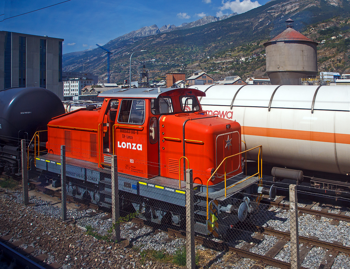 Aus dem Zug heraus, die Em 3/3 163  Rene  (98 85 5837 910-9 CH-LONZA) eine Henschel DHG 500 C der Lonza  AG (Visp), steht am 08.09.2021 in Visp.

Die Henschel  DHG 500 C wurde 1968 von Henschel in Kassel unter Fabriknummer  31239  gebaut und war erst als Mietlok im Einsatz. Im Jahr 1971 verkaufte sie dann Henschel an die Lonza AG in die Schweiz.
2014 wurde die Lok von der LSB Lok Service Balmer AG in Hinwil komplett neu revidiert und remotorisiert.

Die Henschel DHG 500 C ist eine dieselhydraulische Lokomotive, die von den Henschel-Werken gebaut wurde. Sie war vor allem f�r den Einsatz im schweren Werksdienst vorgesehen. Die Lok geh�rt zur ab 1962/63 angebotenen sogenannten vierten Generation der Henschel-Loks, der ersten Generation mit Gelenkwellenantrieb. Die Aufbauten wurden dabei ohne gro�e �nderungen von der vorigen Generation �bernommen.  Zur besseren Bogenl�ufigkeit war die mittlere Achse seitenverschiebbar gelagert. 

Von den Henschel DHG 500 C wurde zwischen 1963 und 1976 insgesamt  62 Exemplaren gebaut. Die Loks gingen vornehmlich an Bergbaugesellschaften und Stahlproduzenten sowie Chemieunternehmen. So erwarb die Rheinelbe Bergbau AG in Gelsenkirchen elf Loks und die Hibernia AG, Zechenbahn- und Hafenbetriebe Ruhr-Mitte in Gladbeck neun Loks vom Typ DHG 500 C. Die meisten Lokomotiven wiesen bei Auslieferung den Henschel-Standardanstrich in Blau mit zwei horizontalen Zierstreifen an den Vorbauten auf. Die durch Zusammenschluss entstandene Ruhrkohle AG hatte zeitweise 31 Lokomotiven dieses Typs im Bestand. 

TECHNISCHE DATEN (nach Umbau):
Spurweite: 	1.435 mm (Normalspur)
Achsformel: C
L�nge �ber Puffer:  9.900 mm
H�he:  4.225 mm
Breite: 3.040 mm
Fester Radstand:  3.700 mm
Kleinster bef. Halbmesser: 	80 m
Dienstgewicht:  60 t
H�chstgeschwindigkeit: 30 km/h / 60 km/h (Schleppfahrt 70 km/h)
Treibraddurchmesser: 	1.000 mm
Motor:  neuer Deutz V6 Motor mit elastischer Vorschaltkupplung. inkl. Partikelfilter (Vollstrombrenner mit aktiver Regeneration), 
der ehemalige Motor war ein Henschel 12V 1416 
Installierte Leistung:  368 kW (500 PS)
Getriebe: Voith
Leistungs�bertragung: hydraulisch (�ber Gelenkwellen)
