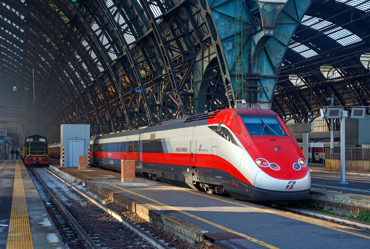 Ausfahrt eines sehr langen  Frecciarossa  (deutsch: roter Pfeil) der Trenitalia (100-prozentige Tochtergesellschaft der Ferrovie dello Stato) am 29.12.2015 vom Bahnhof Milano Centrale (Mailand Zentral). Der Frecciarossa ist eine Zuggattung für Züge mit einer Höchstgeschwindigkeit von 300 km/h. Hier ist es der ETR 500 - 56 ein ETR 500 der 2.Serie. ETR steht ElettroTreno Rapido.

Diese Züge bestehen aus zwei Triebköpfen vom Typ E.404B und aus zwölf Mittelwagen, ETR 500.31 bis 60 komplett der 2.Serie. Bei den ETR 500.01 bis 30 sind nur die beiden Triebköpfe aus der 2.Serie, die Mittelwagen dagegen stammen aus der 1.Serie der ETR 500 (Mono). 

Durch die begrenzte Stromstärke des Gleichstromnetzes können die Hochgeschwindigkeitszüge nur für Geschwindigkeiten bis zu 250 km/h ausreichend mit Energie versorgt werden. Deshalb entschied sich die italienische Staatsbahn in den 1990er Jahren, weitere Neubau-Schnellfahrstrecken mit Wechselstrom (25 kV, 50 Hz) zu betreiben.

Da die erste Serie der ETR 500 nur für das Gleichstromnetz geeignet ist, wurde ab 1996 eine zweite Serie ETR 500 bestellt und geliefert, die sowohl im Gleichstrom- als auch im Wechselstromnetz fahren kann. Die Zweisystem-Fahrzeuge werden Politensione (deutsch: Mehr-Spannung) genannt. Es gab auch mal zwischenzeitlich Dreisystem-Fahrzeuge (ETR 500 F), die auch unter 1.5 kV DC fahren konnten, diese wurden aber wieder zurückgebaut. Diese waren für den Verkehr nach Frankreich gedacht, bekamen aber dort keine Zulassung.

Die zulässige Höchstgeschwindigkeit der ETR 500 der zweiten Serie von 300 km/h wird im regulären Betrieb aber nur mit Wechselstrom auf neueren Schnellfahrstrecken Italiens erreicht.

Im Gegensatz zur ersten Serie werden bei der zweiten Serie Einholmstromabnehmer verwendet. Die Triebköpfe verfügen jeweils über einen Abnehmer für Gleichstrom und einen Abnehmer für Wechselstrom. Äußerlich unterscheiden sich die beiden Bauserien durch starke Unterschiede des „Gesichts“. Die Front der zweiten Serie wurde aufgelockert und rundlicher gestaltet, besonders betont durch die getrennt angeordneten Spitzensignale, während die Frontscheiben kleiner und rechteckig ausgeführt wurden. Wobei ja die Triebköpfe (E.404A) der ersten Serie zu Lokomotiven der Baureihe E.414 umgebaut wurden.


TECHNISCHE DATEN:
Von einem Triebkopf E.404B
Spurweite:  1.435 mm (Normalspur)
Achsformel: Bo'Bo'
Länge: 20.250 mm
Höhe: 4.000 mm
Breite: 3.020 mm
Drehzapfenabstand:  11.450 mm
Achsabstand im Drehgestell: 3.000 mm
Dienstgewicht: 68 t
Höchstgeschwindigkeit: 300 km/h
Dauerleistung: 4.400 kW (4 x 1.100 kW) pro Triebkopf
Treibraddurchmesser:  1.100 mm
Stromsysteme: 3000 V DC und 25 kV 50 Hz AC

Daten der Mittelwagen:
Länge: 26.100 mm
Drehzapfenabstand:  19.000 mm
Achsabstand im Drehgestell: 3.000 mm
Eigengewicht: 40 t

Gesamtzug Daten:
Achsformel: Bo'Bo' (12x 2'2') Bo'Bo'
Gesamtzuglänge: 353.700 mm (bei 12 Mittelwagen)
Gesamteigengewicht: 616 t
Dauerleistung: 8.800 kW
Anfahrzugkraft:  400 kN
