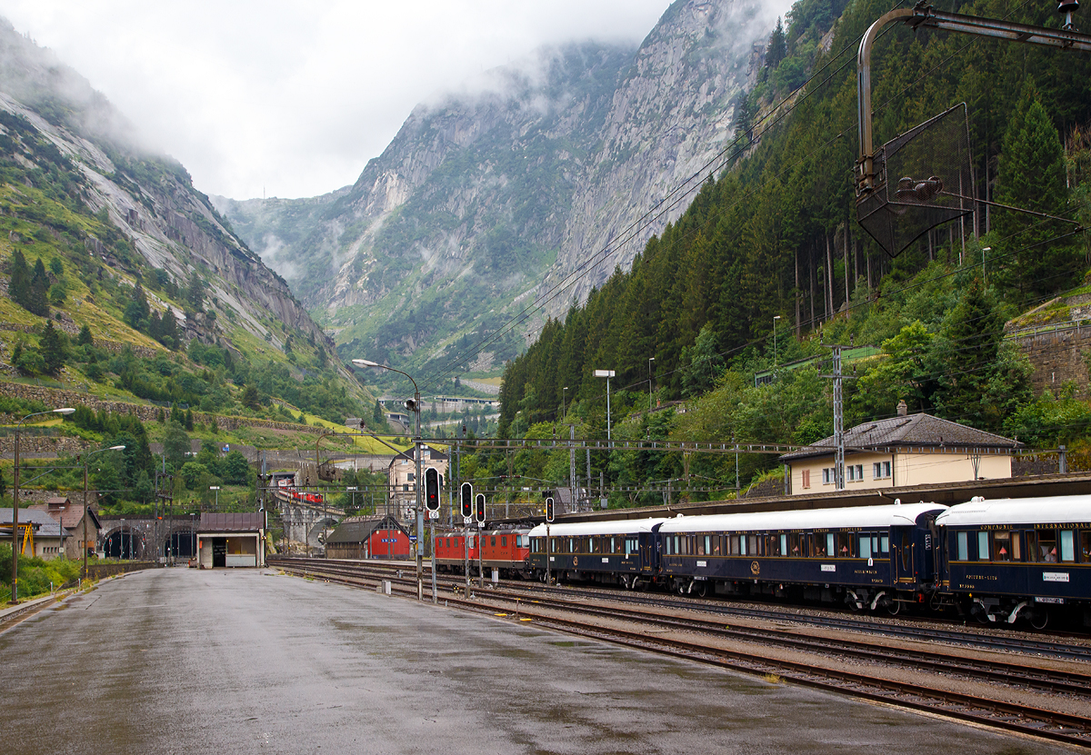 
Bahnhof Göschenen am 02.08.2019:
Während die SBB Re 8/8 (Re 4/4-11194 und Re 4/4-11156) mit dem Venice Simplon-Orient-Express (VSOE) nach Venedig im Bahnhof hält, schiebt eine MGB Deh 4/4 einen Schöllenenbahn-Zug über die Reuss in Richtung Andermatt.

Gut sichtbar (links im Bild die beiden Tunneleingänge), das Nordportal von dem über 100 Jahre alten und ca. 15 km langen Gotthardtunnel (italienisch Galleria del San Gottardo Gotthardtunnel).

Leider war es am regen als der VSOE hielt, aber man kann ja nicht alles verlangen.....