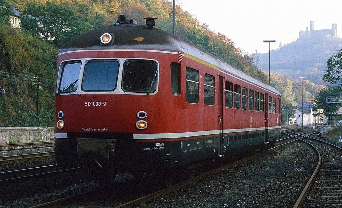 Bereits 1950 dachte man schon an Energieeinsparung....
Im Herbst 1983 der letzte betriebsf�hige Akkutriebwagen der Baureihe 517 (517 008-9) „Limburger Zigarre“ auf Abschiedsfahrt, hier wartet er in Balduinstein auf die R�ckfahrt nach Limburg.

Die Akkumulatortriebwagen der Baureihe ETA 176 waren bei der Deutschen Bundesbahn die Vorl�ufer der Baureihe ETA 150. Aufgrund ihrer wichtigsten Stationierung in Limburg (Lahn) und des neuartigen Aussehens erhielten sie ab etwa 1960 den Spitznamen Limburger Zigarre.

Die Deutsche Bundesbahn zog bereits kurz nach ihrer Gr�ndung im Jahre 1949 in Betracht, Fahrzeuge mit niedrigerem Energieverbrauch zu beschaffen. Hierf�r schien die elektrische Traktion sehr geeignet, die ihre Grenzen jedoch sp�testens auf nicht elektrifizierten Strecken fand. Denn zu dieser Zeit waren viele Hauptstrecken noch nicht elektrifiziert. F�r derartige Strecken wurde ebenfalls versucht, das umfangreiche Personal von mit Dampflokomotiven bespannten Z�gen m�glichst auf eine oder zwei Personen zu beschr�nken. Eine L�sung f�r beide Vorgaben fand die DB in Form ihres ersten selbst in Auftrag gegebenen Akkumulatortriebwagen ETA 176. Es spielten auch die durchweg positiven Erfahrungen der Preu�ischen Staatseisenbahnen und der Deutschen Reichsbahn mit solchen Fahrzeugen (u. a. dem ETA 178) eine gro�e Rolle.

So wurden in den Jahren 1952 bis 1954 insgesamt acht Triebwagen dieser Bauart in Dienst gestellt, die sogar von angelerntem, d. h. nicht zwingenderweise als Lokf�hrer ausgebildetem Personal bedient werden konnten. Als weiterer Kostenvorteil ist zu nennen, dass die Akkutriebwagen keinen Lokschuppen o. �. zum Abstellen oder Warten ben�tigten und einfach im Freien abgestellt werden konnten. �berdies konnten sie auch zur kalten Jahreszeit ohne l�ngere Wartezeiten genutzt werden. Nicht nur die Energie-, sondern auch die Wartungskosten lagen unter denen von Verbrennungstriebwagen.

Im Betrieb �berzeugte der ETA 176 mit seiner hoch bemessenen Anfahrbeschleunigung, welche durch eine Anfahr�berlastung der Motoren erreicht werden konnte. Prinzipbedingt erzeugte er keine Rauch- und kaum Ger�uschbel�stigungen und war sicherheitstechnisch gesehen ungef�hrlicher als Dampfz�ge einzustufen.

Der wesentliche Nachteil dieser Fahrzeuggattung liegt in dem gegen�ber Verbrennungstriebwagen erh�hten Anschaffungspreis und dem Zwang, zugeh�rige Ladeeinrichtungen in ausreichender Zahl bereitzuhalten, da sonst, v. a. auf h�geligen Strecken durch den dadurch h�heren Energiebedarf, verl�ngerte Wartezeiten bis zur n�chsten Einsatzm�glichkeit drohten. Au�erdem wurde der Oberbau untergeordneter Strecken durch die schwergewichtigen eingebauten Bleiakkumulatoren st�rker als bisher belastet. Letzten Endes mussten die Nachteile aber hintenanstehen, und die DB richtete die Eins�tze dieses Akkumulatortriebwagens speziell auf die vorhandenen Ladeeinrichtungen und anderen Verh�ltnisse aus.

Die Konstrukteure mussten f�r diese Quasi-Neuentwicklung zahlreiche Vorgaben erf�llen. Die Triebwagen sollten, wenn sie schon entsprechende Infrastruktur voraussetzen, auf unterschiedlichen Haupt- und Nebenstrecken mit H�chstgeschwindigkeiten zwischen ca. 50 und 90/100 km/h eingesetzt werden k�nnen. Im Nebenbahnbetrieb war v. a. eine hohe Anfahrbeschleunigung zur Verringerung der Fahrzeiten zwischen den zahlreich vorhandenen Bahnh�fen/Haltepunkten, im Einsatz auf den Hauptstrecken eine hohe H�chstgeschwindigkeit sowie in Anzahl und Art ausreichend vorhandene Ein-/Ausstiegseinrichtungen (T�ren) zu verwirklichen. Um den Reisekomfort zu steigern, wurden auch in der dritten Klasse Polster- und mit Kunstleder bezogene Sitze eingebaut, es waren zus�tzliche 50 Stehpl�tze vorhanden.

Es wurde, um dem sich �ber Tag oder Strecke �ndernden Kapazit�tsbedarf gerecht zu werden, eine Vielfachsteuerung eingebaut, mit der ein zweiter Wagen angekuppelt und dessen Steuerabteil f�r den gesamten Zugverband benutzt werden konnte. Eine Akkuladung  reichte je nach Einsatzprofil (Zugart und Strecke) f�r bis zu 400 km. Der Anschluss an eine der station�ren Ladeanlagen erfolgte �ber mehrere, entlang des Triebwagens verteilte Steckdosen, in deren �ffnungen die Stecker der Ladekabel befestigt wurden.

TECHNISCHE DATEN:
Gebaut: je 8 Trieb- und Steuerwagen (ETA 176 / ESA 176)
Spurweite: 1.435 mm (Nornalspur)
Achsformel: Bo'2'(ETA) + 2'2'(ESA)
L�nge: 27.000 mm 
Dienstgewicht: 83,6 t
Radsatzfahrmasse: 16,0 t
H�chstgeschwindigkeit: 90 km/h (001–002) / 100 km/h (003ff.)
Stundenleistung: 2� 100 kW = 200 kW
Beschleunigung: 0,4 m/s�
Reichweite: ca. 400 km
Kapazit�t: 940 Ah
Motorentyp: vierpoliger Reihenschlussmotor vom Typ SSW-GB 190-20
Anzahl der Fahrmotoren: 	2
Antrieb: Tatzlager-Antrieb
Bremse: Knorr, (Druckluft-Klotzbremse)
Kupplungstyp: 	Scharfenberg
Sitzpl�tze: 12 der 1.Klasse und 60 der 2.Klasse (ETA) / 96 der  2.Klasse (ESA)
Fu�bodenh�he: 1.260 mm
