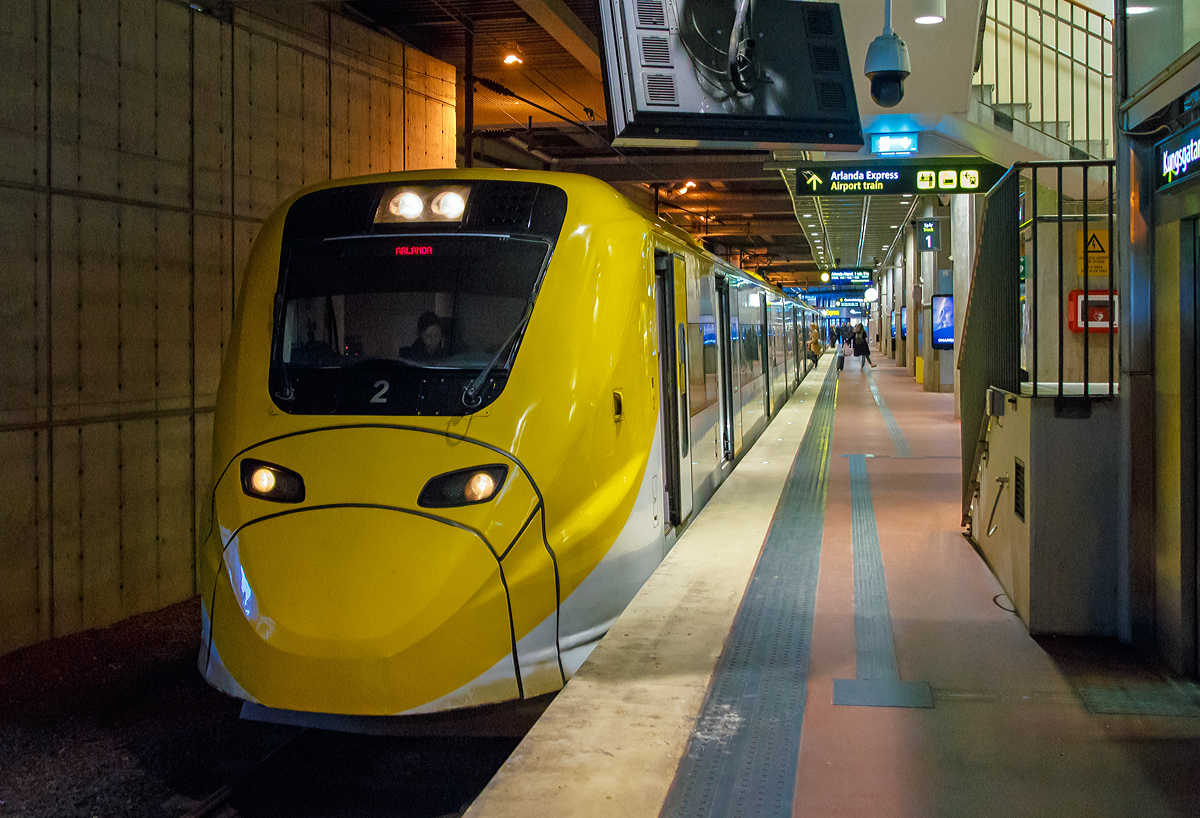 Der Arlanda Express Triebzug 2, ein Alstom Coradia X3, steht am 21.03.2019 auf Gleis 1 in Stockholm Central zur Abfahrt nach dem Flughafen Stockholm/Arlanda bereit.

Der vierteilige, normalspurige elektrische Triebwagenzug vom Typ X3 wird von der schwedischen Gesellschaft Arlanda Express f�r den direkten Verkehr zwischen Stockholm C und Flughafen Stockholm/Arlanda verwendet.

Von Alstom wurden sieben dieser klimatisierten Z�ge in Birmingham gebaut und 1998/99 geliefert. Der X3 geh�rt zur Obergruppe der Coradia-Triebwagen und kann Geschwindigkeiten bis 205 km/h erreichen. Die Z�ge sind wei� und gelb lackiert. Die Triebwagen nutzen das gleiche Stromsystem, wie es im gesamten schwedischen Eisenbahnnetz vorhanden ist.

TECHNISCHE DATEN:
Spurweite: 1435 mm (Normalspur)
Achsformel: Bo'Bo'+2'2'+'2'2+Bo'Bo'
L�nge �ber Kupplung: 93.084 mm
Dienstgewicht: 187 t
H�chstgeschwindigkeit: 200 km/h
Leistung: 2.240 kW
Stromsystem: 15 kV 16 2/3 Hz ~
Sitzpl�tze: 228

Arlanda Express ist eine schwedische Bahnverbindung, die mit dem 200 km/h schnellen Elektrotriebzug X3 seit 1999 den Stockholmer Hauptbahnhof mit dem Flughafen Stockholm/Arlanda verbindet. Die Z�ge bew�ltigen die Strecke in 20 Minuten. Am Flughafen bedienen sie die Stationen Arlanda S�dra und Arlanda Norra. Die Z�ge verkehren bis auf wenige Ausnahmen in den Tagesrandzeiten alle 15 Minuten, im Berufsverkehr etwa alle zehn Minuten.

In Arlanda und im Hauptbahnhof von Stockholm am Gleis 1 und 2 haben die Z�ge gesonderte Bahnsteige. Dort ist ein direkter stufenloser �bergang vom Zug zum Bahnsteig m�glich. Jeder Wagen verf�gt �ber zwei T�ren und an jeder T�r sind Gep�ckablagen vorhanden. Der gesamte Zug besitzt 190 Sitzpl�tze. In einem der Wagen sind gesonderte Pl�tze f�r Rollstuhlfahrer sowie ein WC vorhanden.

