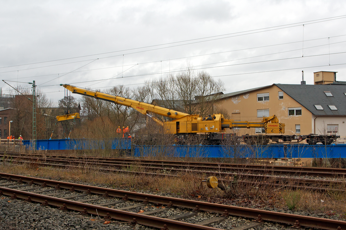 
Der KSW Bahnhof Siegen-Eintracht (Betriebsbereich Eisern-Siegener Eisenbahn), ist von den DB Gleisen (der Siegstrecke KBS 460) durch die Sieg getrennt. Am Bahnhof Siegen-Eintracht befindet sich auch der Hauptsitz der KSW mit Werkstätten, zudem auch die neue Werkstatt der HLB. So ist die eingleisige Siegbrücke die Nabelschnur der KSW Kreisbahn Siegen-Wittgenstein GmbH (KSW) zwischen dem Bahnhof Eintracht und dem Hauptbahnhof Siegen. Die bisherige Brücke war in ihrem Ursprung über 130 Jahre alt und wurde zuletzt 1982 instand gesetzt, aber auf Grund des Alters war ihre Standfestigkeit nicht mehr gewährleistet. Deshalb war auch die maximal erlaubte Geschwindigkeit nur noch Schritttempo. Nun erfolgte der Neubau der Brücke und Auflager, wobei die vorhanden zwei Betonpfeiler überarbeitet wurden. Die Konstruktion ist ein offenes, gekrümmtes Trägerrost in Stahlbauweise mit direkter Schienenbefestigung auf den Längsträgern und damit der bisherigen Brücke sehr ähnlich. Die Kosten für die Sanierung der Siegbrücke belaufen sich auf schätzungsweise rund 1,6 Mio. €, die Hälfte davon trägt der Bund.

So wurde am 20.12.2014 der Brückenoberbau mit Hilfe von dem 150 t Kirow Gleis- und Weichenbaukran KRC 1200+ (ein Kirow MULTI TASKER KRC 1200+) 99 80 9419 005-0 D-STRA  „DONAU“  (ex 97 82 55 508 17-5) der STRABAG RAIL GmbH gesetzt. Der Kran ist hier gekoppelt mit dem Gegenlastwagen 99 80 9 320 001-7 D-STRA. Durch die Lastablegung (Gegengewicht) auf Gegengewichtswagen im Kranbetrieb erfolgt eine Achslastreduzierung.

TECHNISCHE DATEN von dem Kran:
Spurweite: 1.435 mm
Eigengewicht  (in Transportstellung) : 111,0 t 
Länge über Puffer:  15.000 mm  (+13.000 mm Gegenlastwagen)
Motorleistung:  254 kW bei 2.200 U/min
max. Geschwindigkeit im Zugverband: 100 km/h
max. Geschwindigkeit im Eigenantrieb: 19 km/h
Achsanzahl:  8 (in 4 Drehgestelle bzw. 2 Doppeldrehgestelle)
Drehzapfenabstand: 10.000 mm
Drehzapfenabstand im Drehgestell 1 und 2: 2.300 mm
Achsabstand in den Einzeldrehgestellen: 1.100mm
Ergebene Achsabstände in m: 1,1 / 1,2 / 1,1/ 6,6 / 1,1 / 1,2 / 1,1
Achsfolge: 1'A'1A'A1'A1'
Radsatzlast Transport Kran: max. 13,8 t
Radsatzlast Gegengewichtswagen:  max. 20,0 t
Höhe in Transportstellung:  4.300 mm
Breite in Transportstellung:  3.100 mm
max. Ausladung vor Puffer:  21.000 mm
max. Traglast bei max. Ausladung:  40 t
Größte mögliche Traglast: 150 t (abgestützt)  / 120t (freistehend)
max. Hakenhöhe:  24.000 mm
hintere Ausladung (Gegenwicht):  7,9 m–13,5 m
Zul. Anhängelast: 160 t
Kleinster befahrbarer Radius: 80 m (120 m im Schleppbetrieb)


Besondere Ausstattung:
Überhöhenausgleich 180 mm
Schwenkradius ± 360º
Abstützung teleskopierbar bis 8 m Abstützbasis
profilfreies Arbeiten bis ± 30º

Der Kran wurde 2009 von Kirow in Leipzig unter der Fabriknummer 152500 gebaut. Er wird als Schweres Nebenfahrzeug Nr.: 99 80 9419 005-0 (ehemals 97 82 55 508 17-5) geführt und hat die EBA-Nr. EBA 09C02A001. 
