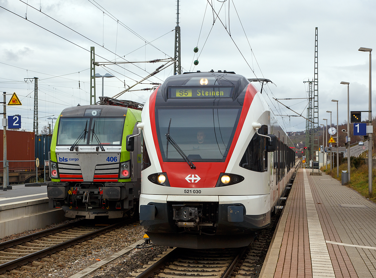 
Der Stadler Flirt RABe 521 030   R�publique et Canton du Jura  der SBB GmbH steht am 28.12.2017 im Bahnhof Weil am Rhein, als S5 nach Steinen via L�rrach, auf Gleis 1 zur Abfahrt bereit. Er bef�hrt die Bahnstrecke Weil am Rhein–L�rrach  Gartenbahn  (KBS 734) und ab L�rach die  Wiesentalbahn  (KBS 735). 

Auf Gleis 2 fahren gerade zwei Re 475 der BLS Cargo durch.