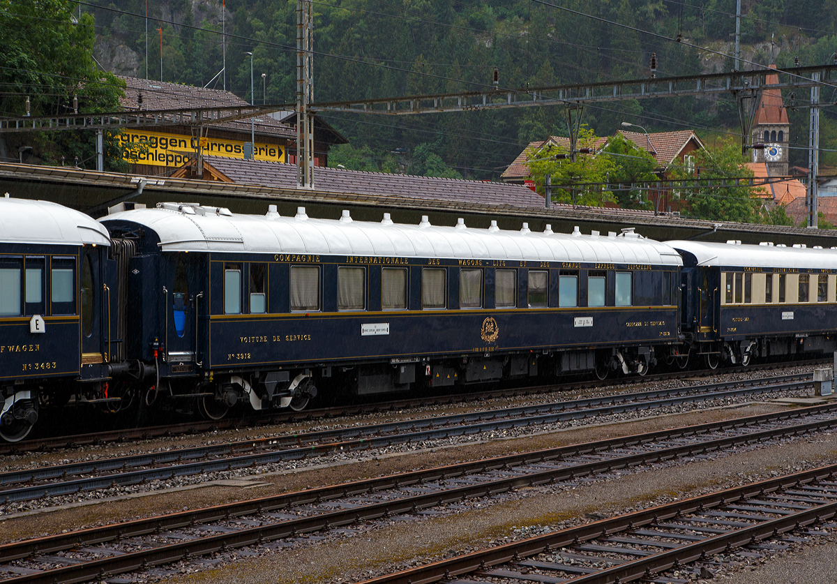 Der VSOE Service- und Personalschlafwagen Nr. 3912 (F- VSOE 61 87 06-70 912-7), ex CIWL 3912 Schlafwagen vom YTp (ex CIWL 51 66 06-41 339-6) im Zugverbund vom Venice Simplon-Orient-Express am 02.08.2019 beim Halt in G�schenen (CH), leider bei Regen.

Der Servicewagen, ein ehemaliger CIWL Typ YTp Schlafwagen wurde 1949 von der Soci�t� anonyme des Ateliers M�tallurgiques in Nivelles (Belgien) gebaut und als Schlafwagen (WL) vom Typ YTp an die CIWL geliefert die ihn als Nr. 3912 bezeichnete. Ende der 1970er-Jahre wurde er an die VSOE verkauft. Die VSOE lie� den Wagen durch die Bremer Waggonbau GmbH (ehem. Hansa Waggonbau) 1982 zum Service- und Personalschlafwagen umbauen. 

Beide Service-Wagen (Voiture de Service / Carrozza di Service) Nr. 3912 und 3915 vom Typ YU der VSOE haben Schlafabteile f�r das Personal (mit jeweils 14 Betten), Gep�ck- und Vorratsr�ume f�r die Speisewagen, sowie ein Kohlelager f�r Kohle befeuerten Heiz�fen der Schlafwagen.

Zwischen 2003 und 2006 wurde die Wagen der VSOE nochmals modernisiert und erhielten unter anderem moderne Drehgestelle von Bombardier. Durch die neuen Drehgestelle sind die Wagen seitdem f�r 160 km/h zugelassen.

TECHNISCHE DATEN:
Spurweite: 1.435 mm (Normalspur)
Anzahl der Achsen: 4 in zwei Drehgestellen
L�nge �ber Puffer: 23.452 mm
Drehzapfenabstand: 16.000 mm
Achsabstand im Drehgestell: 2.500 mm
Eigengewicht: 52 t
H�chstgeschwindigkeit: 160 km/h (urspr�nglich 140 km/h)
Bettpl�tze f�r Personal: 14