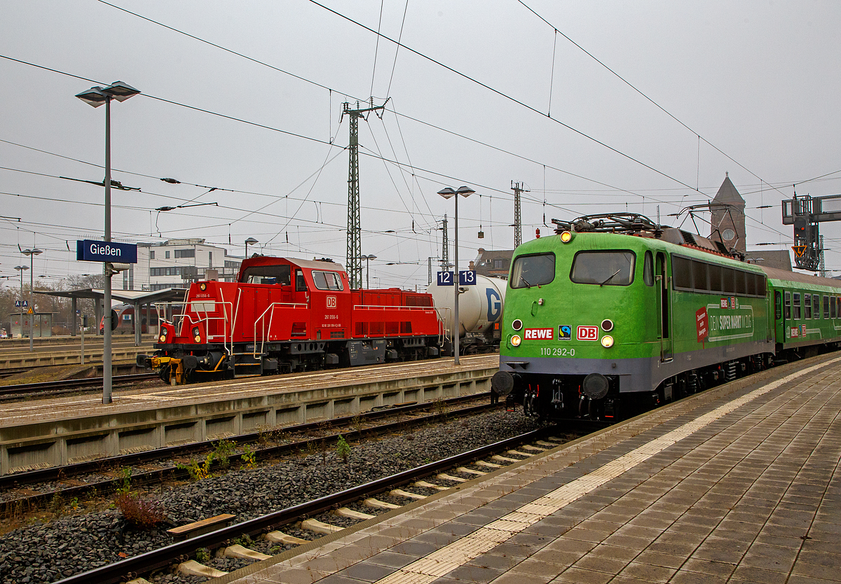 Die 261 056-6 (92 80 1261 056-6 D-DB) eine Voith Gravita 10 BB der DB Cargo AG, kam am 12.11.2021 mit einem Kesselwagenzug von den Oberhessischen Strecken, der Lahn-Kinzig-Bahn (KBS 631) oder Vogelsbergbahn (KBS 635), in Gießen an und hatte kurz Hp 0. Nun geht es auf die Main-Weser-Bahn (KBS 630). Rechts steht die Bügelfalten E10, die 110 292–0 (91 80 6110 292-0 D-GfF) der Gesellschaft für Fahrzeugtechnik mbH mit dem REWE - Supermarkt-Zug.

Die Voith Gravita 10 BB wurde 2011 unter der L04-10107 gebaut und ausgeliefert.
