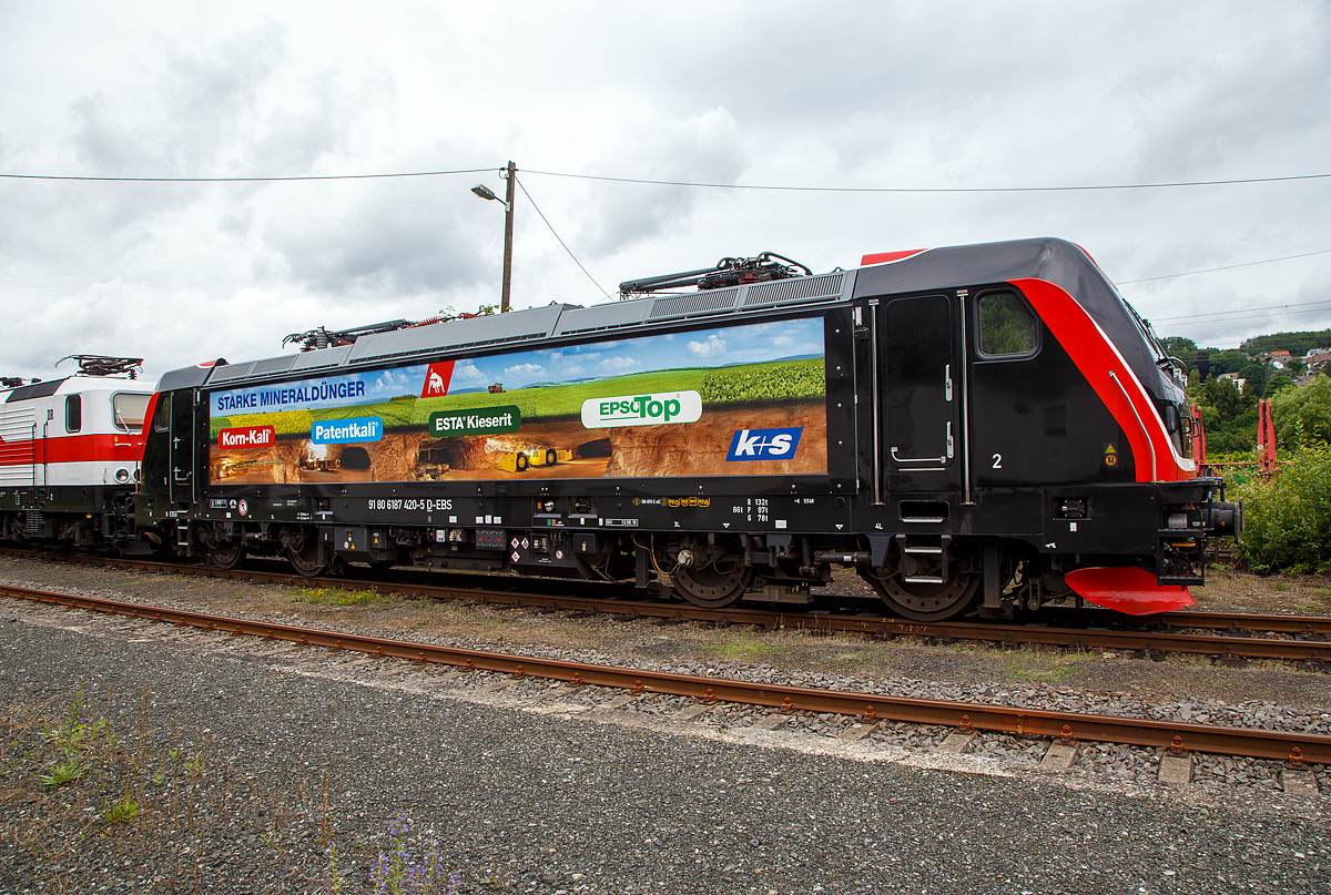 Die Bombardier TRAXX F160 AC3 LM, 187 420-5 (91 80 6187 420-5 D-EBS) der EBS - Erfurter Bahnservice GmbH steht am 05.07.2021 in Scheuerfeld (Sieg) beim Kleinbahnhof der WEBA (Westerwaldbahn), für ihre nächste Aufgabe der Abfuhr von schweren Holzzügen, bereit.

Die Bombardier TRAXX F160 AC3 LMD wurde 2019 von Bombardier in Kassel unter der Fabriknummer 35595 gebaut. Nach meiner Sichtung hat die Lok die Zulassung für Deutschland (D) und Österreich (A). Für Ungarn und Rumänien sind die Zulassungen noch nicht erteilt (H und RO sind durchgestrichen).

Wie die Vorgängerinnen AC1 und AC2 ist die AC3 für den Betrieb unter 15 Kilovolt bei 16,7 Hertz, sowie unter 25 Kilovolt bei 50 Hertz Wechselstrom ausgelegt, und verfügt unverändert über eine Dauerleistung von 5.600 kW und eine Anfahrzugkraft von 300 kN. Von den Traxx 2E übernommen wurde der Maschinenraum mit Seitengang um das sogenannte Powerpack, bestehend aus Stromrichter und Hochspannungsgerüst, womit erstmals alle Varianten dasselbe Layout verwenden.

Neu ist die Kopfform der Traxx-3-Lokomotiven, im Wesentlichen ein auf dem Lokkasten aufgesetztes GFK-Modul. Zudem wurden die Lokomotiven erstmals ab Werk konstruktiv für den Einbau der Zugbeeinflussung ETCS vorbereitet. Neuerungen betreffen die verfügbaren Drehgestelle: zu den bisherigen Varianten „F140“ mit Tatzlagerantrieb und Zulassung für maximal 140 km/h, und „P160“ mit Hohlwellenantrieb und Zulassung für maximal 160 km/h, werden die Traxx-3-Lokomotiven offiziell auch als Variante „F160“ mit Tatzlagerantrieb und Zulassung für maximal 160 km/h angeboten.

Gänzlich neu sind die optional verfügbaren Last-Mile-Module, die es als Last-Mile-Diesel (LMD) mit zusätzlicher Last-Mile-Battery (LMB) gibt. Das LMD besteht aus einem Dieselhilfsmotor und einem Kraftstofftank, um auch nicht-elektrifizierte Streckenabschnitte und Anschlussgleise befahren zu können. Der Dieselmotor von Deutz verfügt über einen Hubraum von 7.150 cm³, erbringt eine Leistung von 230 kW (180 kW am Rad), mit Batterieunterstützung 290 kW und erfüllt die Stage-IIIB-Abgasnorm. Im Dieselbetrieb werden alle vier Fahrmotoren betrieben, die Anfahrzugkraft beträgt dabei mit Batterieunterstützung unverändert 300 kN, ohne Batterie 260 kN. Ohne Anhängelast ist damit eine Höchstgeschwindigkeit von 60 km/h möglich, bei 2000 Tonnen Last noch 40 km/h. Der Tankinhalt von 400 Litern reicht für bis zu acht Stunden Dieselbetrieb, kurze Strecken können auch ausschließlich mit der eingebauten Batterie zurückgelegt werden. Der Übergang vom elektrischen zum Dieselbetrieb kann während der Fahrt erfolgen. Für den Rangierbetrieb ist zudem eine Funkfernsteuerung erhältlich.

Erstmals wurde der Lokkasten nicht mit glatten Seitenwänden gefertigt, sondern konstruktiv deutlich günstiger, sind die Seitenwände der AC3 vertikal gesickt und die Seitenflächen erhielten sogenannte Flex-Panels, eine Vorrichtung zum Einspannen von Planen. Diese würden die Sicken verdecken, und wären kostengünstiger als Umlackierungen oder Umbeklebungen. Die Nutzung der Flex-Panels wurde jedoch in der Schweiz umgehend untersagt.

TECHNISHE DATEN:
Hersteller:  Bombardier Transportation
Spurweite:  1.435 mm (Normalspur)
Achsanordnung: Bo’ Bo’
Länge über Puffer: 18.900 mm
Drehzapfenabstand: 10.440 mm
Achsabstand im Drehgestell: 2.600 mm
Treibraddurchmesser:  1.250 mm (neu) / 1.170 mm (abgenutzt)
Höhe:  4.283 mm
Breite:  2.977 mm
Lichtraumprofil: UIC 505-1
Dienstgewicht:  87 t
Fahrmotoren: 4 Asynchronmotoren
Bremse: Elektrische Bremse (SW-GPR-E mZ)

Daten im Oberleitungsbetrieb:
Höchstgeschwindigkeit: 160 km/h
Dauerleistung: 5.600 kW 
Kurzzeitleistung  Power Boost : 6.000 kW
Anfahrzugkraft: 300 kN
Dauerzugkraft: 252 kN bei 80 km/h
Stromsystem:  15 kV 16,7 Hz~ und 25 kV 50 Hz~

Daten im Dieselbetrieb (Last-Mile):
Nenndrehzahl: 1.800 U/min
Höchstgeschwindigkeit:  60 km/h
Dauerleistung: 230 kW (180 kW am Rad),
Tankinhalt:  400 l