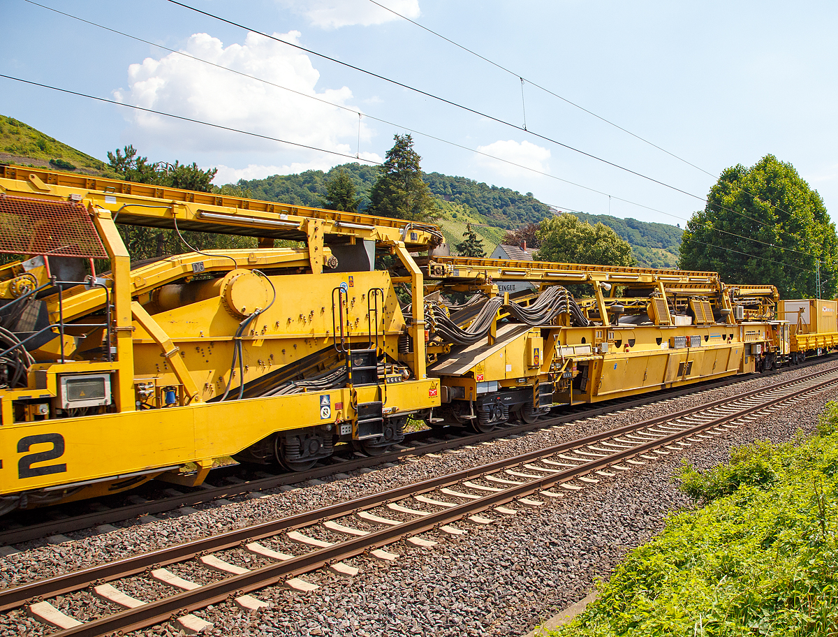 
Die Wiebe Recycling-Planumsverbesserungsmaschine mit Schotterrecycling RPMW 2002-2 am 14.07.2018 im Zugverband auf der Fahrt durch Leutesdorf,  auf der KBS 465 (Rechte Rheinstrecke) in Richtung Norden. 

Über 140 Meter lang, knapp 5 Meter hoch und gute 560 Tonnen schwer – die Gleisbaumaschine RPMW 2002-2 gehört zu den größten der Welt. Mit ihrer beachtlichen Leistung und dem umfänglichen Leistungsspektrum ist sie ein äußerst wichtiger Bestandteil des Maschinenparks der Unternehmensgruppe Wiebe.

Die Recycling Planumsverbesserungsmaschine führt verschiedene Gleisbauarbeiten durch – und das mit einer Motorengesamtleistung von über 2100 Kilowatt. Diese Kraft kommt bei Totalsanierungen zum Tragen, bei denen die RPMW 2002-2 mehrere Arbeitsschritte simultan ausführt: Die verschmutzte Schotterbettung wird ausgebaut, das abgetragene Bettungsmaterial aufbereitet, Schotter recycelt und die Unterbauplanumsschicht erneuert.

TECHNISCHE DATEN:
Hersteller: Plasser & Theurer
Baujahr, Erstzulassung: 2000
Spurweite: 1.435 mm
Anzahl der Achsen: 29, davon 12 angetrieben
Baumaschinennummer: Aushubmaschine 3369, Recyclingmaschine 3368, Antriebswagen 3367,  Stopf- u. Einschotterungsmaschine 3370
Motoren: Caterpillar 
Leistung: 2.860 PS
Gesamtlänge über Puffer: 140,90 m
Breite: 3,29 m
Höhe: 4,65 m
Gewicht: 560 t
V zul. im Zug eingestellt: 100 km/h
V max. bei Eigenfahrt: 20 km/h
Fahrradius: 120 m

Der große Unterschied zwischen Planumsverbesserungsmaschine und Bettungsreinigungsmaschinen besteht darin, dass die Planumsverbesserungsmaschine nicht nur den Schotter ausheben und recyceln kann, sondern auch einen Teil des Planums (Unterbau) ausheben (bis 1.200 mm unter SOK). Zudem kann die RPM vor der Neuschotterung (Recycling- mit Neumaterial) auch eine Planumsschutzschicht (PSS-Material) einbringen.
Der Neuschottern wird durch die Stopfeinrichtung 09-32 Stopfsatellit im Gleisbett verdichtet und das Gleis ist danach wieder mit 70 km/h befahrbar.

Hier im Bild ist der Anfang der Maschine (in Arbeitsrichtung), wo aber nicht der erste Arbeitsschritt beginnt, denn der beginnt an der Schotteraushubkette. Im Betrieb werden Materialförder- und Siloeinheit en (MFS) vor die Maschine gesetzt, zwei Förderbänder der Maschine ausgefahren und der Abraum in die MSF übergeben.