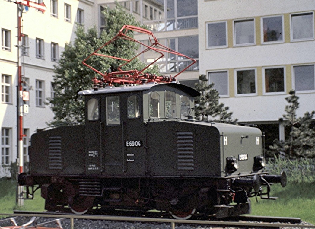 E 69 04 in M�nchen auf einem Sockel vor der Oberpostdirektion, aus einem ge�ffneten Oberlicht einer fahrenden Strassenbahn fotografiert, am 26.05.1979 (Diascan).
