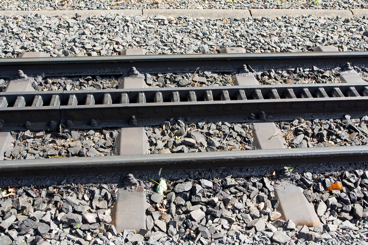Gleis der Drachenfelsbahn am 06.06.2014 in K�nigswinter an der Talstation. 

Das Gleis ist komplett auf Stahlschwellen verlegt, die Spurweite betr�gt 1.000 mm (Meterspur). 
Das Zahnstangensystem ist Riggenbach (Leiterzahnstange), nach ihrem Erfinder Niklaus Riggenbach. Zwischen zwei U-f�rmigen Profilen sind die Z�hne als Sprossen eingesetzt, die Zahnteilung betr�gt 100 mm, (urspr�nglich genietet, heute geschwei�t). Diese Bauart l�sst sich mit einfachen Mitteln fertigen, erfordert aber f�r Kurven Spezialanfertigungen, da sich die fertige Zahnstange nicht biegen l�sst. Weichen wurden daher als Schiebeweichen, bei denen ein Gleisabschnitt verschoben wird, ausgef�hrt, w�hrend heute konventionelle Weichen in Verbindung mit Zahnstangen des Systems von Roll zur Anwendung kommen (dies ist auch bei der Drachenfelsbahn der Fall).
