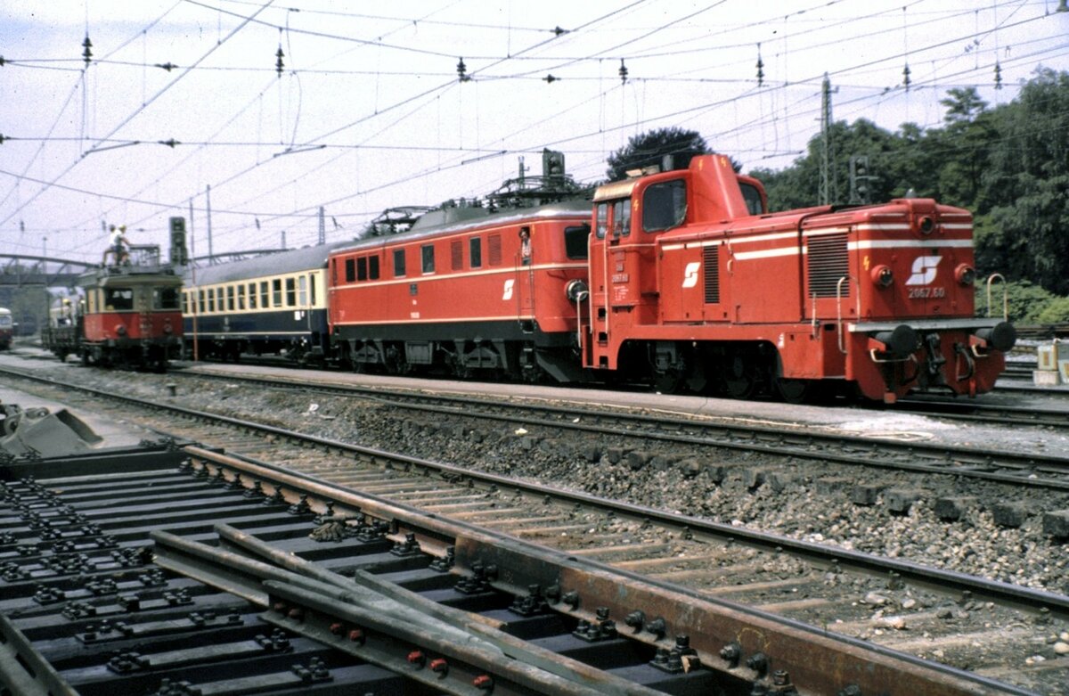 �BB 2067.60 schleppt 1110.06 mit Zug aus stromlosen Bereich; im Hintergrund befindet sich ein Turmtriebwagen X 534 im Arbeiteinsatz in Bregenz am 12.06.1983.