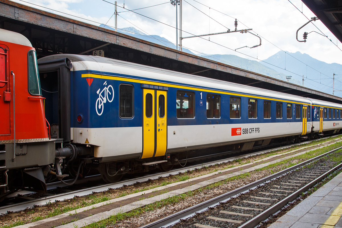 
SBB – 1.Klasse Personenwagen A 50 85 18-35 029-5, ein modernisierte Einheitswagen I (EW1), eingereiht in einem Pendelzug am 05.08.2019 im Bahnhof Domodossola.

Die Einheitswagen I sind die Nachfolger der Leichtstahlwagen und wurden zwischen 1956 und 1967 gebaut. Sie waren ursprünglich in SBB-Grün lackiert und hatten ein Gewicht von 28 bis 32 Tonnen, eine Länge von 23,7 m und eine zulässige Höchstgeschwindigkeit von 140 km/h.

Damit die Einstiege über den Drehgestellen angeordnet werden konnten, mussten die Drehgestellrahmen in der Mitte gekröpft ausgeführt werden. 

Die Senkfenster sind einteilig, einfach verglast und rahmenlos; die Scheiben werden beim Öffnen bis zur Hälfte in die Wagenseitenwand versenkt.

Über 360 Einheitswagen I wurden ab 1984 für die Neuen Pendelzüge (NPZ) umgebaut. Sie bekamen eine Lackierung nach dem NPZ-Schema (weiss-blau mit gelben Türen), entsprechende Sitzpolsterung und eine neue Inneneinrichtung. Automatische Türen (außenbündig) für den kondukteurlosen Betrieb wurden in einem zweiten Schritt ab 1992 eingebaut. Diese Wagen werden im Regionalverkehr sowohl als NPZ wie auch mit t Re 4/4 II eingesetzt. Dazu wurden auch alle Steuerwagen mit Personenabteilen der Einheitstypen I und II entsprechend umgebaut. 

Während per 2018 die Einheitswagen II fast vollständig ausrangiert sind, sind im Gegensatz noch viele Einheitswagen I im Dienst.

TECHNISCHE DATEN:
Spurweite: 1.435 mm (Normalspur)
Länge über Puffer: 23.700 mm
Drehzapfenabstand: 17.600 mm
Achsabstand im Drehgestell: 2.700 mm
Eigengewicht: 32 t
Sitzplätze: 60 in der 1.Klasse und Fahrradabteil
Bremse: O-R 43t (P43t) K