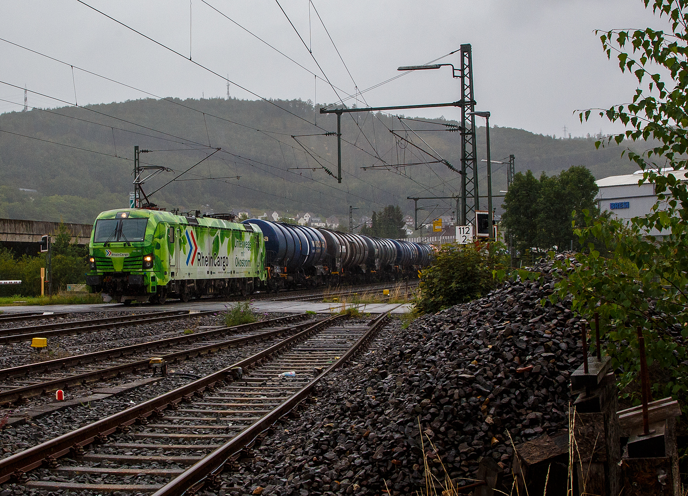 Bei Regen „Unterwegs mit �kostrom“, die SIEMENS Smartron 192 031-3 (91 80 6192 031-3 D-RHC), bzw. Lok 3001 der RheinCargo GmbH & Co. KG f�hrt man 03.08.2023 mit einem sehr langen Kesselwagenzug durch Niederschelden in Richtung K�ln. Die Ladung der Kesselwagen war laut Gefahrgutkennzeichnung (30/1202) Dieselkraftstoff beziehungsweise leichtes Heiz�l.

Die Smartron wurde 2020 von Siemens Mobilitiy in M�nchen-Allach unter der Fabriknummer 22889 gebaut. 

