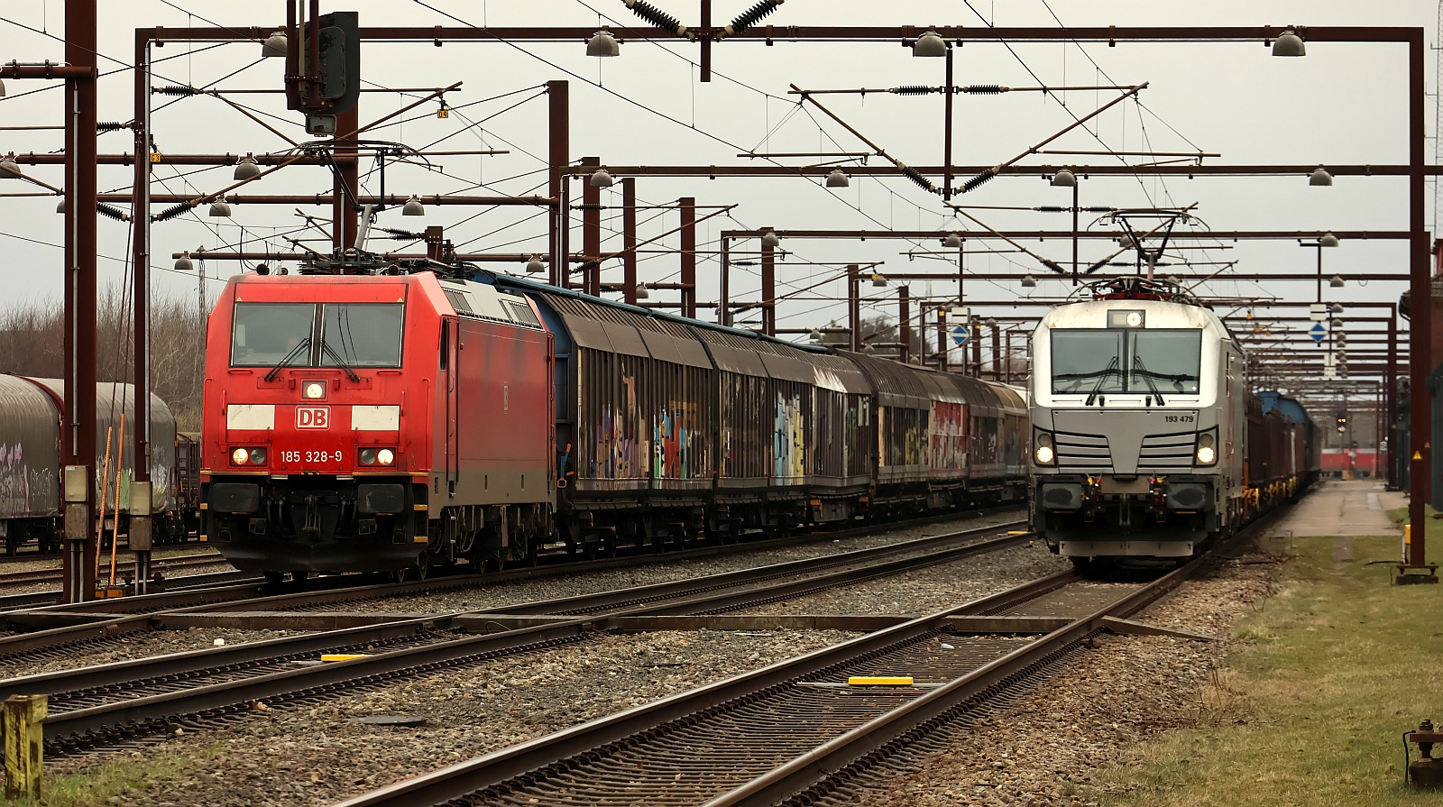 DBCSC 185 328-9 REV/AM9/18.05.24 mit H-Wagen Zug die kurz nach ihrer Ankunft gegen die 185 331 ausgetauscht wurde und 193 479 mit ihrem Güterzug warten auf Ausfahrt im Bhf Padborg/DK 13.03.2026