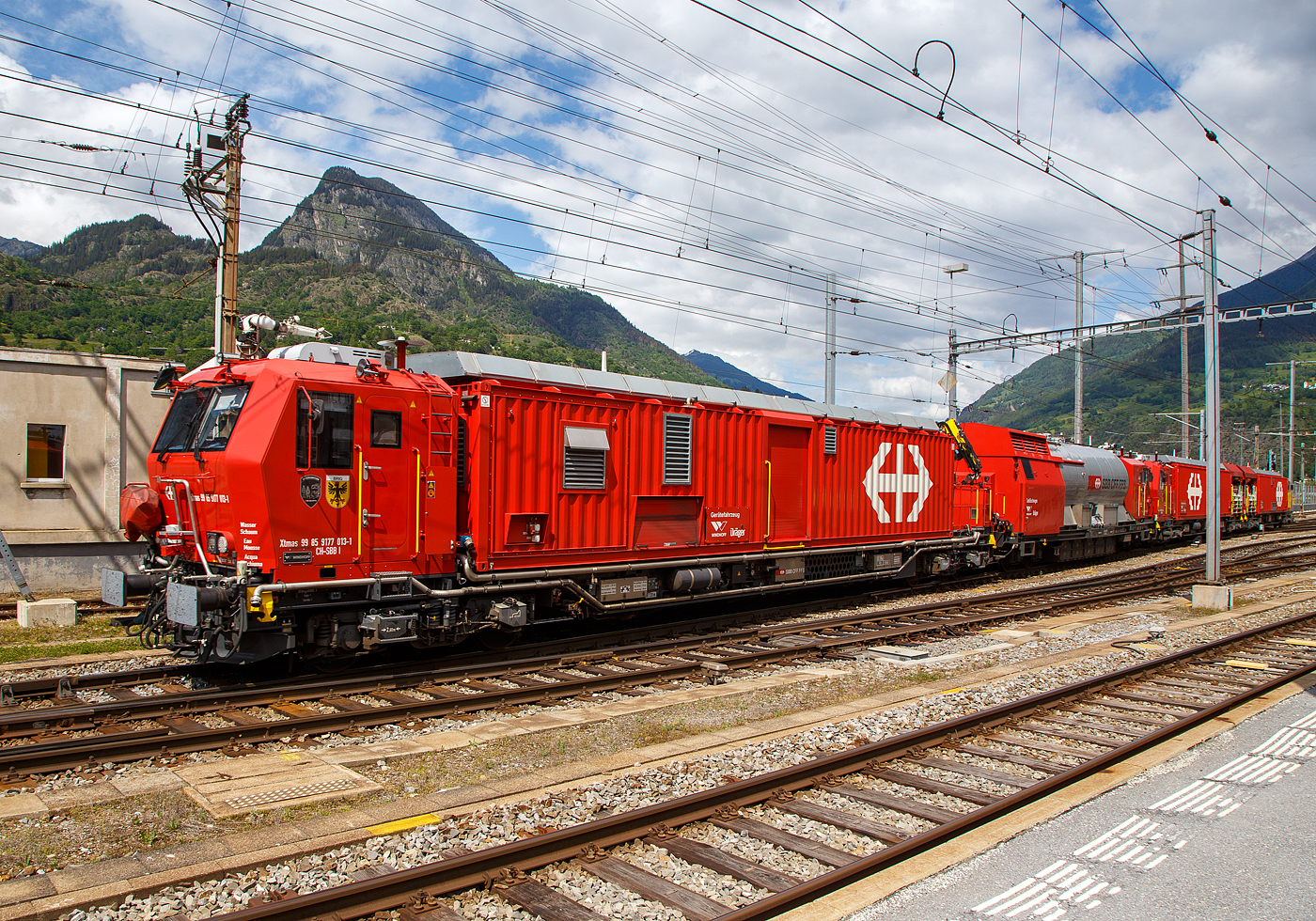 Der 4-teilige L�sch- und Rettungszug „Brig“ (ein vierteiliger LRZ 18) der SBB Infrastruktur erreicht am 25 Mai 2023 seinen Heimatbahnhof Brig.

Der L�sch- und Rettungszug wurde 2018 f�r die SBB Infrastruktur, Depot Brig, gebaut und besteht aus dem:
Rettungsfahrzeug 1 - Xtmas 99 85 9174 023-3 CH-SBBI;
Rettungsfahrzeug 2 - Xtmas 99 85 9174 013-4 CH-SBBI;
Tankl�schwagen - Xans 99 85 9375 013-1 CH-SBBI; sowie
Ger�tefahrzeug - Xtmas 99 85 9177 013-1 CH-SBBI

Die neuste Generation der L�sch- und Rettungsz�ge (LRZ 2018) ist vierteilig und besteht aus einem Tankl�schwagen, einem Ger�tefahrzeug und zwei Rettungsfahrzeugen. Der Antrieb erfolgt mit je zwei MTU-Dieselpowerpacks (6-Zylinder Turbo geladener Dieselmotor von MTU, Partikelfilter, Turbogetriebe mit eingebauten Retarder und K�hlsystem) nach EU-Abgas-Emissionsstufe IIIA Norm, mit je 390 kW Leistung �ber die beiden Rettungs- sowie das Ger�tefahrzeug. Der L�sch- und Rettungszug hat so eine installierte Gesamtleistung von 2.340 kW (6 x 390 kW), eine H�chstgeschwindigkeit von 100 km/h und kann Anh�ngelasten von 940 Tonnen bei einer Steigung von 27 Promille bewegen, in der Ebene sogar mit einem Gewicht von �ber 1.600 t. 

Der Tankl�schwagen ist nicht selbstfahrend, er ist als Steuerwagen ausgef�hrt, daher auch die Gattungsbezeichnung Xans. Er besitzt zwar einen Deutz 6-Zylinder- Dieselmotor (mit 238 KW Leistung) mit vollautomatischem Partikelfilter, einer und angeflanschtem Pumpenaggregat von Vogt, dieser wird aber nur Wasser- und Schaummittelpumpen ben�tigt.

Der gesamte Atemluftvorrat des Zuges betr�gt 1.980.000 Normliter und wird in 132 Speicherflaschen, die ein Volumen von 50 Litern haben, mit 300 Bar Druck gelagert. An verschiedenen Orten in den Innenr�umen und auf den Plattformen sind Anschl�sse f�r die Atemluftversorgung vorhanden. Daran k�nnen separate Atemschutzmasken oder das tragbare Atemschutzger�t mit Geber- und Nehmerschlauch angeschlossen werden. Alle F�hrerstandkabinen sind druckdicht und verf�gen �ber eine Atemluftversorgung, welche einen �berdruck erzeugt. In den F�hrerstandkabinen des Ger�tefahrzeugs und des Tankl�schwagens ist zus�tzlich ein Bedienpult f�r die Feuerl�schtechnik eingebaut.

Zwischen 4 und 5 Stunden  ist ein autonomer Betrieb des LRZ m�glich.

Im Einsatz wird der Zug in zwei Einheiten geteilt. Die erste Einheit aus Ger�tefahrzeug und Tankl�schwagen (mit 780 kW Antriebsleistung) dient der Feuerbek�mpfung und dem Bergungsarbeiten. Die zweite Einheit (mit 1.560 kW Antriebsleistung), bestehend aus zwei Rettungsfahrzeugen �bernimmt im Shuttleverkehr den Personentransport zu einem sicheren Ort.

Quellen: SBB und Anschriften
Stand (�berarbeitung): September 2025

