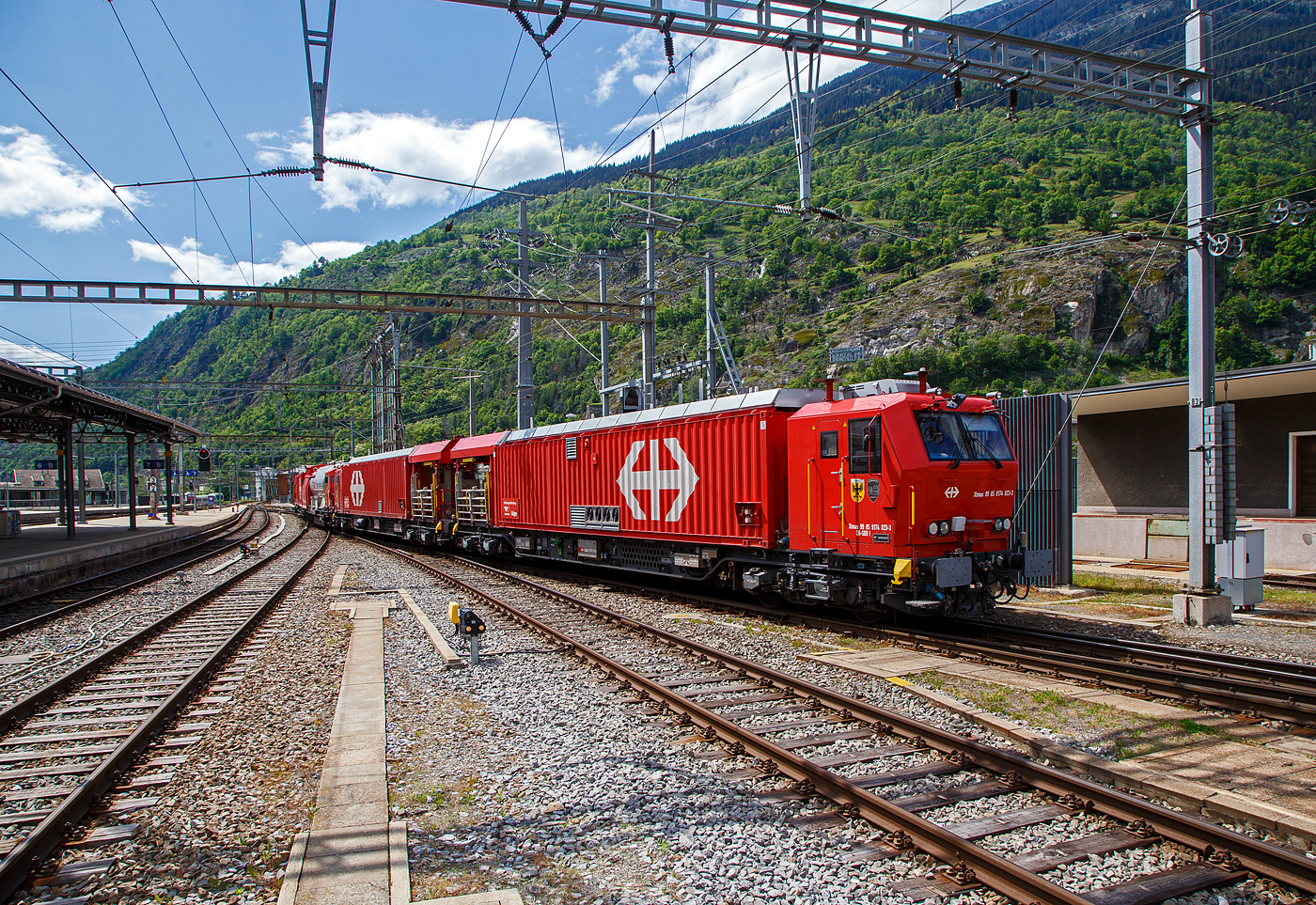 Der 4-teilige L�sch- und Rettungszug „Brig“ (ein vierteiliger LRZ 18) der SBB Infrastruktur erreicht am 25 Mai 2023 seinen Heimatbahnhof Brig.

Der L�sch- und Rettungszug wurde 2018 f�r die SBB Infrastruktur, Depot Brig, gebaut und besteht aus dem:
Rettungsfahrzeug 1 - Xtmas 99 85 9174 023-3 CH-SBBI;
Rettungsfahrzeug 2 - Xtmas 99 85 9174 013-4 CH-SBBI;
Tankl�schwagen - Xans 99 85 9375 013-1 CH-SBBI; sowie
Ger�tefahrzeug - Xtmas 99 85 9177 013-1 CH-SBBI

Die neuste Generation der L�sch- und Rettungsz�ge (LRZ 2018) ist vierteilig und besteht aus einem Tankl�schwagen, einem Ger�tefahrzeug und zwei Rettungsfahrzeugen. Der Antrieb erfolgt mit je zwei MTU-Dieselpowerpacks (6-Zylinder Turbo geladener Dieselmotor von MTU, Partikelfilter, Turbogetriebe mit eingebauten Retarder und K�hlsystem) nach EU-Abgas-Emissionsstufe IIIA Norm, mit je 390 kW Leistung �ber die beiden Rettungs- sowie das Ger�tefahrzeug. Der L�sch- und Rettungszug hat so eine installierte Gesamtleistung von 2.340 kW (6 x 390 kW), eine H�chstgeschwindigkeit von 100 km/h und kann Anh�ngelasten von 940 Tonnen bei einer Steigung von 27 Promille bewegen, in der Ebene sogar mit einem Gewicht von �ber 1.600 t. 

Der Tankl�schwagen ist nicht selbstfahrend, er ist als Steuerwagen ausgef�hrt, daher auch die Gattungsbezeichnung Xans. Er besitzt zwar einen Deutz 6-Zylinder- Dieselmotor (mit 238 KW Leistung) mit vollautomatischem Partikelfilter, einer und angeflanschtem Pumpenaggregat von Vogt, dieser wird aber nur Wasser- und Schaummittelpumpen ben�tigt.

Der gesamte Atemluftvorrat des Zuges betr�gt 1.980.000 Normliter und wird in 132 Speicherflaschen, die ein Volumen von 50 Litern haben, mit 300 Bar Druck gelagert. An verschiedenen Orten in den Innenr�umen und auf den Plattformen sind Anschl�sse f�r die Atemluftversorgung vorhanden. Daran k�nnen separate Atemschutzmasken oder das tragbare Atemschutzger�t mit Geber- und Nehmerschlauch angeschlossen werden. Alle F�hrerstandkabinen sind druckdicht und verf�gen �ber eine Atemluftversorgung, welche einen �berdruck erzeugt. In den F�hrerstandkabinen des Ger�tefahrzeugs und des Tankl�schwagens ist zus�tzlich ein Bedienpult f�r die Feuerl�schtechnik eingebaut.

Zwischen 4 und 5 Stunden  ist ein autonomer Betrieb des LRZ m�glich.

Im Einsatz wird der Zug in zwei Einheiten geteilt. Die erste Einheit aus Ger�tefahrzeug und Tankl�schwagen (mit 780 kW Antriebsleistung) dient der Feuerbek�mpfung und dem Bergungsarbeiten. Die zweite Einheit (mit 1.560 kW Antriebsleistung), bestehend aus zwei Rettungsfahrzeugen �bernimmt im Shuttleverkehr den Personentransport zu einem sicheren Ort.

Quellen: SBB und Anschriften
Stand (�berarbeitung): September 2025

