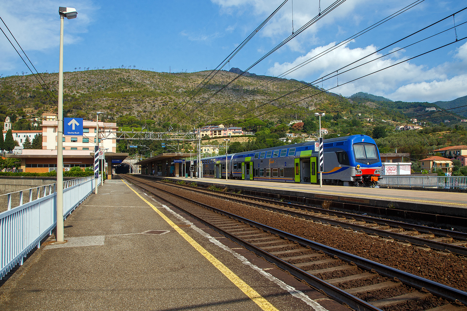 Der Bahnhof Levanto an der Italienischen Riviera (nördlich der Cinque Terre) an der Bahnstrecke Pisa–Genua (RFI Strecke-Nr. 77 / KBS 31 La Spezia–Genua) am 23.07.2022.

Steuerwagen voraus steht hier ein Trenitalia „Vivalto“- Doppelstock-Wendezug, als Cinque Terre Express nach La Spezia, zu Abfahrt bereit. Vorne der Trenitalia „Vivalto“-Steuerwagen 50 83 26-78 957-7 I-TI der Gattung npBH, am Zugschluss war die Trenitalia E.464 578, eine Bombardier TRAXX P160 DCP.

In den letzten Jahren werden bei Trenitalia für RegioExpress-Züge die Vivalto-Wagen eingesetzt, Zuglok ist meist eine E.464 (Bombardier TRAXX P160 DCP). Einige Wagen sind auch bei Trenord und den Ferrovie Emilia Romagna zu finden. Von dieser zweite Serie der CDPTR-Wagen (Carrozza Double Deck for Regional Transport) wurden 350 Wagen ab 2012, gebaut von AnsaldoBreda / Hitachi Rail Italy, in Dienst. Die sechsteiligen Doppelstock-Wendezüge haben eine Kapazität von etwa 1.000 Fahrgästen, darunter 700 Sitzplätze und ein Fahrradabteil. 

Nach der Einführung der neuen DPR-Lackierung bei den Elektrozügen ETR 425  Jazz , basierend auf grau mit blau/orangefarbenen Bändern und grünen Türen, wurde die gleiche Lackierung auch auf andere Fahrzeuge des Fuhrparkeres für Regionalzüge der Trenitalia ausgedehnt, einschließlich der modernen Doppelstockwagen  Vivalto .

Das „Vivalto“-Logo in der Mitte der Seitenteile blieb zunächst auch in der neuen Lackierung unverändert, allerdings mit einem Farbwechsel für die horizontale Linie, um besser mit dem neuen grafischen Design zu harmonieren.