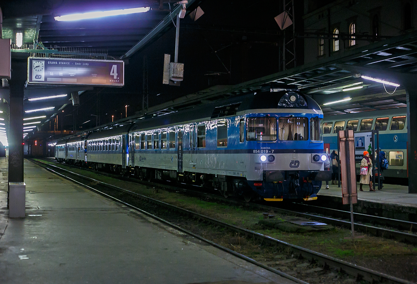 Der Dieseltriebwagen ČD 854 019-7 „Babička“ (Oma) (CZ-ČD 95 54 5 854 019-7) hat am 22.11.2022, mit einem Regionalzug bzw. als  Esko Praha (S-Bahn Prag), Praha Masarykovo nádraží (Prag Masaryk Bahnhof) erreicht. Der Zug bestand aus der Komposition  ČD 854 019-7,  Bdtn756, ČD 854 und Steuerwagen ČD ABfbrdtn795 

Die ČD-Baureihe 854 ist ein vierachsiger Dieseltriebwagen (in Achsfolge B'2') der Tschechischen Bahnen (ČD) für den Schnell- und Eilzugverkehr auf den nichtelektrifizierten Hauptstrecken in Tschechien. Sie entstanden im Rahmen eines Rekonstruktionsprogrammes aus Fahrzeugen der Baureihen 852 (vormals ČSD Baureihe M 296.2) und der Baureihen 853 (vormals ČSD Baureihe M 296.1).

Die überalterte Maschinenanlage machte eine Erneuerung der Fahrzeuge unumgänglich. Zwischen 1997 und 2006 wurden 50 Fahrzeuge von der Firma PARS in Šumperk umgebaut. Nach der Rekonstruktion erhielten die Fahrzeuge die Baureihen-Bezeichnung 854. Die Rekonstruktion umfasste die Erneuerung der Maschinenanlage mit Motor, Getriebe, den Fahrgastraum und die Elektrik des Fahrzeuges. Sie erhielten einen neuen Caterpillar-Motor 3412 E DI-TA, der bessere ökologische und Verbrauchswerte besitzt sowie zuverlässiger arbeitet als der bisherige KS 12 V 170 DR. Als Getriebe erhielt der Wagen den Typ H 750 M von ČKD.

Obwohl bei der Rekonstruktion die Inneneinrichtung komplett demontiert wurde, blieben der Grundriss und der Fahrzeugaufbau der Reihen 852 und 853 erhalten. Geändert wurde die Bestuhlung des Fahrzeuges nach dem Muster der Neubautriebwagen 843. Außerdem hat der Triebwagen nach der Rekonstruktion eine automatische Türschließeinrichtung und eine Anzeige für Bedarfshalte erhalten. Die Motorsteuerung wird über eine Mikroprozessorsteuerung als automatisierte Regelung der Geschwindigkeit realisiert. Ebenfalls elektrisch gesteuert ist die Bremse nach dem System DAKO.

Die rekonstruierten Triebwagen der Reihe 854 sind bestimmt für den Personen-. Eil- und Schnellzugdienst auf hochwertigen nichtelektrifizierten Strecken der ČD.. Es wurden und werden auch einige Wagen zu Steuerwagen der Bauart Bfbrdtn794 oder ABfbrdtn795 umgebaut, die allerdings im Unterschied zu den Triebwagen nur einen Führerstand besitzen. Zu den Einsatzstellen der Fahrzeuge siehe die Weblinks.

Die Fahrzeuge besitzen jetzt bessere Traktionseigenschaften, wesentlich erhöht wurden Reisekultur und Arbeitsbedingungen für den Lokführer.

Die ehemalige Baureihe 853 erhielt nun die neue Baureihenbezeichnung 854, wobei die Ordnungsnummern beibehalten wurden. Die ehemalige Baureihe 852 erhielt ebenfalls die neue Baureihenbezeichnung 854 und die Ordnungsnummer wurde um 200 erhöht. So kann man gut erkennen ob es ein ex BR 853 oder BR 852 ist. Alle Fahrzeuge der neuen Baureihe 854 erhielten Namen, wie z.B. „Babička“ (Oma).

Der Antriebsstrang:
Der Dieselmotor ist wassergekühlter V-Zwölfzylinder- Viertakt-Dieselmotor mit Direkteinspritzung und zwei Abgasturboladern und Ladeluftkühlung. Die Kühlventilatoren werden jetzt von Elektromotoren angetrieben. Das Gerät wird von modernen elektronischen Geräten gesteuert, die Motorschutz und Diagnose umfassen. Über eine flexible Kupplung und eine Kardanwelle ist der Diesel mit dem originalen hydrodynamischen Getriebe ČKD H 750 M verbunden, das in einem neuen Gusseisenkasten untergebracht und unter dem Gepäckraum aufgehängt ist. Das Getriebe wurde im Zusammenhang mit der Installation eines neuen Steuerungssystems teilweise modifiziert. Das Getriebe ist hydrodynamisch mit drei Wandlern (ein Wandler zum Anfahren und zwei zum Fahren), automatischem Schalten und Wenden. Das Drehmoment vom Getriebe wird über eine Gelenkwelle auf das Original-Achsgetriebe NP 18 am inneren Rad des Antriebsfahrwerks übertragen. Über dieses Getriebe wird das Achsgetriebe NK 18 angetrieben, das sich an der äußeren Achse des Fahrgestells befindet. Der Triebwagen ist mit einer Handbremse, einer automatischen Druckbremse des DAKO-Systems und einer Direktbremse ausgestattet.

TECHNISCHE DATEN der BR 854:
Hersteller (Umbau): Pars Nova in Šumperk (gehört zu Škoda)
Spurweite: 1.435 mm (Normalspur)
Achsformel: 2' B' 
Länge über Puffer: 24.790 mm
Wagenkastenbreite: 2.883 mm
Höhe: 4.200 mm
Drehzapfenabstand: 17.200 mm
Achsabstand im Drehgestell: 2.400 mm
Treib- und Laufraddurchmesser: 920 mm (neu) / 840 mm (abgenutzt)
Leergewicht: 50.300 kg
Dienstgewicht: 59,1 t
Radsatzfahrmasse:  17,3 t
Höchstgeschwindigkeit: 120 km/h
Dieselmotor: Caterpillar wassergekühlter V-Zwölfzylinder- Viertakt-Dieselmotor mit Direkteinspritzung und zwei Abgasturboladern und Ladeluftkühlung, vom Typ 3412 E DI-TA
Motorhubraum: 27 Liter (Zylinder-Ø 137 mm / Kolbenhub 152 mm)
Nenndrehzahl: 1.650 U/min (Leerlaufdrehzahl 600 U/min)
Installierte Leistung: 588 kW
Anfahrzugkraft: 80 kN
Getriebe: ČKD H 750 M
Leistungsübertragung: hydromechanisch
Sitzplätze: 48
Max. Tankinhalt: 1.600 l
Kleinster befahrbarer Gleisbogen: R 120 m
