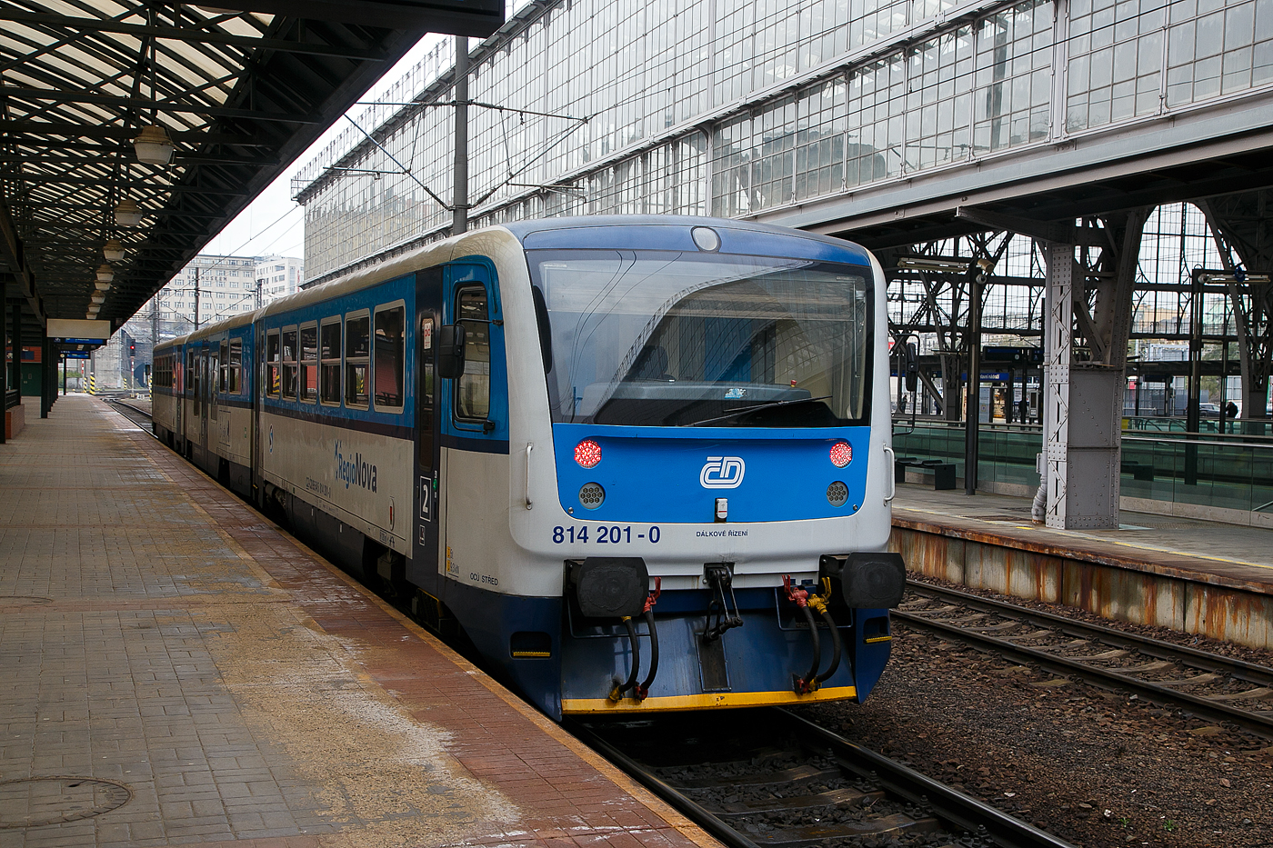 Der RegioNova „Trio“ 814 201-0 / 014 0xx / 814 202-9 steht am 23.11.2022 als Regionalzug im Hauptbahnhof Prag (Praha hlavní nádraží) zur Abfahrt bereit.

Diese dreiteiligen Fahrzeuge der ČD-Baureihe 814.2/014/814.2 entstanden im Rahmen eines Rekonstruktionsprogrammes (2007 bis 2012) aus den Fahrzeugen der ČD-Baureihe 810 bzw. Beiwagen der Reihe 010. Von den ČD werden sie als „RegioNova“ vermarktet.Der Einsatz des Fahrzeuges ergibt vor allem Energieeinsparungen, eine höhere Traktionsgeschwindigkeit und dadurch eine Straffung der Fahrpläne. 

Die Baureihe 814.2:
Eine Weiterentwicklung der Baureihe 814.0 ist die Baureihe 814.2. Eine Einheit besteht anstatt aus einem Motor- und einem Steuerwagen aus zwei Motorwagen (BR 814.2) und einem Mittelwagen (BR 014). Die dreiteiligen Züge bieten 127 Sitzplätze anstatt bei den zweiteiligen Wagen 76. Triebwagen der Baureihe 814.2 sind seit 2007 im Einsatz.

Technische Merkmale:
Wesentliche Veränderungen gegenüber der Ursprungsbauart sind eine neue, leistungsfähigere Antriebsanlage mit dem Dieselmotor LIAZ ML 640 SE (TEDOM TD 242 RH TA25) und dem hydromechanischen Getriebe VOITH DIWA 864.3E, eine bequemere Innenausstattung mit behindertengerechter Toilette, bessere Arbeitsbedingungen für den Lokführer, bessere Fahreigenschaften und geringere Umweltauswirkungen der Antriebsanlage. Die Regionova sind nach wie vor mit Schraubenkupplung ausgerüstet und somit mit anderen Fahrzeugen freizügig kuppelbar.

Im Mittelwagen (BR 014), der zwischen den Radsätzen einen Niederflurbereich auf etwa 50 % der Wagenlänge aufweist, befinden sich das Traglastenabteil, eine Auffahrrampe für Rollstühle, die Toilette und 31 Sitzplätze. Der Einstieg liegt in diesem Bereich in Wagenmitte. Der Triebwagen, in normaler Bodenhöhe aufgebaut, besitzt Fahrgastabteile mit 48 Sitzplätzen. Die Antriebsanlage liegt wie bei der Ursprungsbauart unter dem Wagenboden, auch die Lage der Einstiege wurde bei den Triebwagen nicht verändert.

Beschreibung von Škoda:
Die Zuggarnituren entstehen durch eine Rekonstruktionen und Modernisierung der ursprünglichen Wagen, die in den Jahren 1973-1983 hergestellt wurden. Der Hauptbeitrag der Rekonstruktion ist neben der Erhöhung der Qualität des Reisens auf den Regionalstrecken auch die Reduzierung der Kosten für den Betrieb und die Wartung.

Die modernisierten Einheiten haben einen geringeren Verbrauch und in den Endstationen müssen sie nicht umgespannt werden. Der Zug Regionova  Trio  besteht aus zwei Triebwagen und einem Niederflur-Zwischenwagen, der die Beförderung von Personen mit eingeschränkter Mobilität und von Eltern mit Kinderwagen erleichtert.. In den Zuggarnituren ist genügend Platz auch für größeres Gepäck. Eine komplette Modernisierung machte auch der Zugführerraum durch.

TECHNISCHE DATEN Regionova „Trio“:
Hersteller (Umbau): Pars Nova in Šumperk (gehört zu Škoda)
Spurweite: 1.435 mm (Normalspur)
Achsformel: 1'A' + 1'1' + A'1'
Länge über Puffer: 42.410 mm
Wagenkastenbreite: 3.073 mm
Höhe: 3.420 mm
Leergewicht: 62,3 t
Radsatzfahrmasse: 9,75 t
Höchstgeschwindigkeit: 80 km/h
Installierte Leistung: 242 kW (bei 1.950 U/min)
Anfahrzugkraft: 54 kN
Motorentyp: 2x TEDOM TD 242 RH TA25 (LIAZ ML 640 SE)
Getriebe: 2 x Voith Diwa 864.3E
Leistungsübertragung: hydromechanisch
Sitzplätze: 127
Fußbodenhöhe: 570 mm (Niederflurteil)
Kleinster befahrbarer Gleisbogen: R 120 m
Bremse: DK-P
