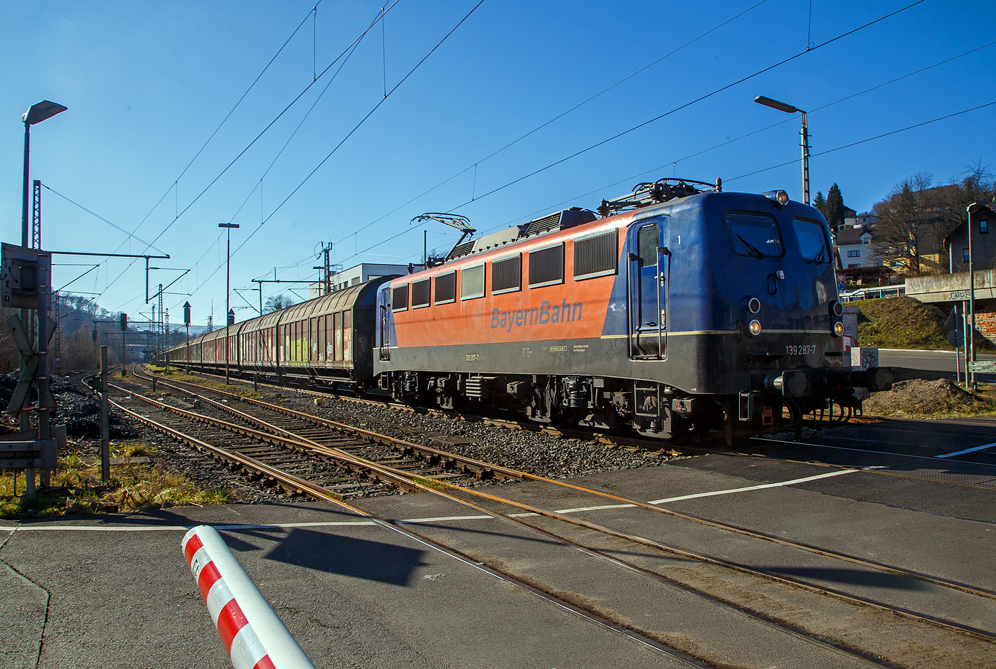 Die 139 287-7 (91 80 6139 287-7 D-BYB) der BayernBahn GmbH f�hrt am 14.02.2023 mit dem sogenannten  Henkelzug  (Langenfeld/Rhld. nach Gunzenhausen), durch Niederschelderh�tte, hier beim B� 343 (km 112,183) kurz vor Niederschelden bzw. der Landesgrenze zu NRW, in Richtung Siegen. Der Zug bestand aus gedeckten Schiebewand-Wageneinheiten der Gattung Hiirrs, sowie drei Kesselwagen und als Schlussl�ufer die 275 817-5 der Alpha Trains.

Nochmal einen lieben Gru� an den netten Lokf�hrer zur�ck.

Die Lok wurde 1963 von Krauss-Maffei AG in M�nchen-Allach unter der Fabriknummer 18956 gebaut, er elektrische Teil ist von den Siemens-Schuckert-Werke (SSW) in Berlin. Als DB E10 287 wurde in Dienst gesetzt, mit der Einf�hrung des EDV-Nummernsystems wurde sie zum 01.01.1968 zur DB 110 287–0. Die Lok ist mit Einholmstromabnehmern ausger�stet, sie ist die letzte gebaute Kasten 110er. Zur 139er wurde sie erst 1994 nach einem Umbau, der Lokkasten wurde auf Drehgestelle der Baureihe 140 (E40) gesetzt und es folgte die Umzeichnung in DB 139 287-7. Zum Mai 2009 erfolgte die Z-Stellung bei der DB AG. Zum 1.Oktober 2011 wurde die Lok durch die BayernBahn GmbH erworben und erhielt anschlie�end eine Untersuchung. Die Neulackierung in kobalt-blau/orange erhielt sie dann 2017.
