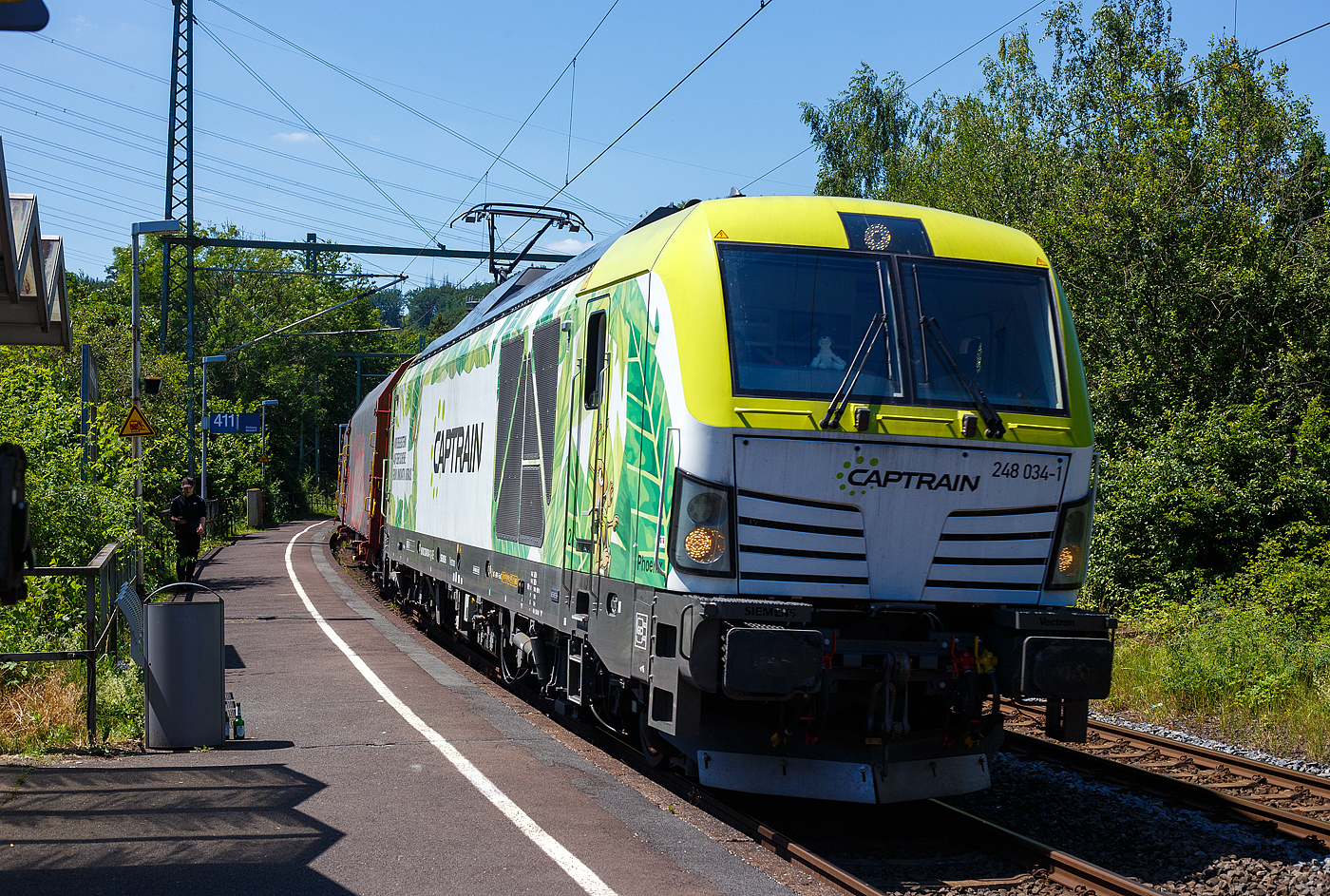 Die an die Dortmunder Eisenbahn GmbH (DE) vermietete SIEMENS Vectron Dual Mode 248 034-1  Phoenix  (90 80 2248 034-1 D-DE) der Captrain Deutschland GmbH fährt am 25 Juni 2024, mit einem Coilzug (Wagen der Gattung Shimmnis-ttu der Ermewa) durch den Bahnhof Scheuerfeld/Sieg in Richtung Siegen. 

Die SIEMENS Vectron DM wurde 2022 von Siemens Mobility GmbH in München-Allach unter der Fabriknummer 23185 gebaut und im Februar 2023 an die Captrain ausgeliefert. Die Lok hat die Zulassung für Deutschland und eine Höchstgeschwindigkeit von 160 km/h. Die Hybridlok (Vectron Dual Mode) kann die Antriebsenergie aus der Fahrleitung beziehen (2.400 kW Leistungen am Rad), oder mittels eines MTU 16V 4000 R84 V16-Zylinder-Dieselmotors (2.400 kW Motorleistung, 2.000 kW Leistungen am Rad) erzeugen. 

Die Dortmunder Eisenbahn GmbH (DE) ist eine private Eisenbahngesellschaft aus Dortmund. Die Dortmunder Eisenbahn GmbH ist ein gemeinsames Tochterunternehmen der Dortmunder Hafen GmbH und der Captrain Deutschland GmbH. Sie ist zu 65 Prozent im Besitz der Captrain Deutschland GmbH (deutsche Tochter der SNCF) und 35 Prozent der Anteile hält die Dortmunder Hafen AG. Die DE Infrastruktur GmbH,  mit ca. 50 Kilometern Gleislänge, gehört zu 81 Prozent der Dortmunder Hafen AG und zu 19 Prozent der Captrain Deutschland GmbH.
