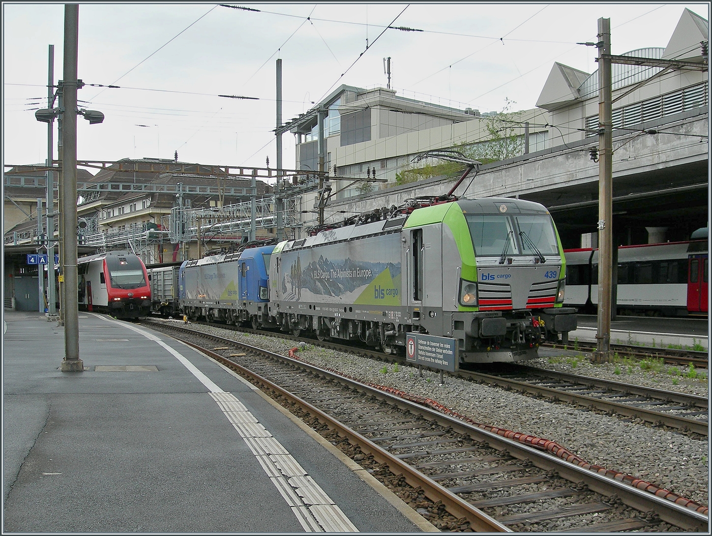 Die BLS Re 475 439 (91 85 4475 439-6 CH-BLSC) und die 193 496 (91 80 6193 496-7 D-BLSC) wartet in Lausanne mit einem langen Zug aus Sgmmns M29 Wagen die Block Distanz zum ausfahrenden IR 90 (ganz links im Bild) ab. 

5. Mai 2026