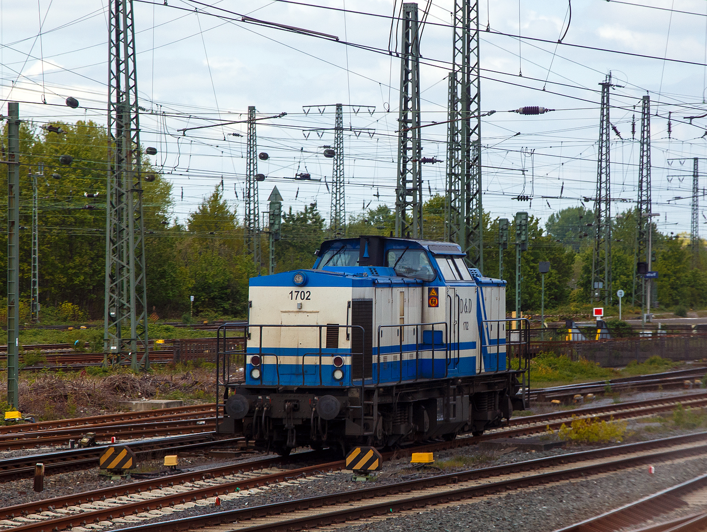 Die D&D 1702 bzw. 203 130-0 (92 80 1203 130-0 D-DUD) der D&D Eisenbahngesellschaft mbH (Hagenow), ex DB 202 602-9, ex DR 112 602-8, ex DR 110 602-0, steht am 30.04.2022 beim Bahnhof Hamm (Westf.). Aufnahme aus dem Zug heraus.

Die Diesellok eine DR V 100.1 wurde 1973 von LEW (VEB Lokomotivbau Elektrotechnische Werke „Hans Beimler“, Hennigsdorf) unter der Fabriknummer 13920 gebaut und als DR 110 602-0 an die Deutsche Reichsbahn ausgeliefert. 1984 erfolgte bereits eine Remotorisierung/Umbau im Bw Meiningen und die Umzeichnung in DR 112 602-8. Zum 01.01.1992 erfolgte die Umzeichnung in DR 202 602-9 und zum 01.01.1994 dann DB AG. Die Ausmusterung bei der DB erfolgte 1999. Im Jahre 1998 ging sie an die SFZ - Schienenfahrzeugzentrum Stendal. Von der ALS - ALSTOM Lokomotiven Service GmbH in Stendal erfolgte dann 2002 der Umbau gemäß Umbaukonzept  BR 203.1  in die heutige 203 130-0. Im Jahr  2007 wurde sie an die D&D Eisenbahngesellschaft mbH (Hagenow) verkauft.