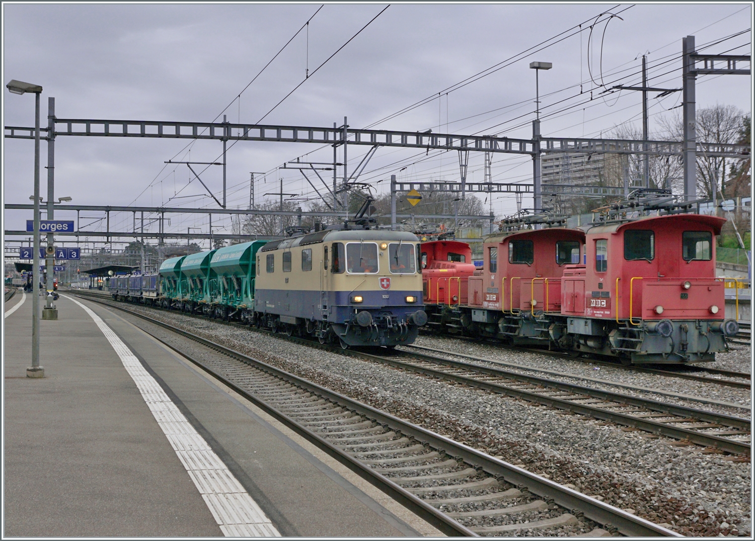 Die  IRSI Rheingold Re 4/4 II 11387 (Re 421 387) ist in Morges mit ihrem Kieszug von Gland angekommen und beginnt nun das Manöver, indem der Zug dann auf die Rollbockanlage geschoben wird. Neben der Lok stehen zwei BAM MBC Te 2/2 (Te 212) und (neu) der Tem III (97 85 1220 329-7. 

4. März 2024