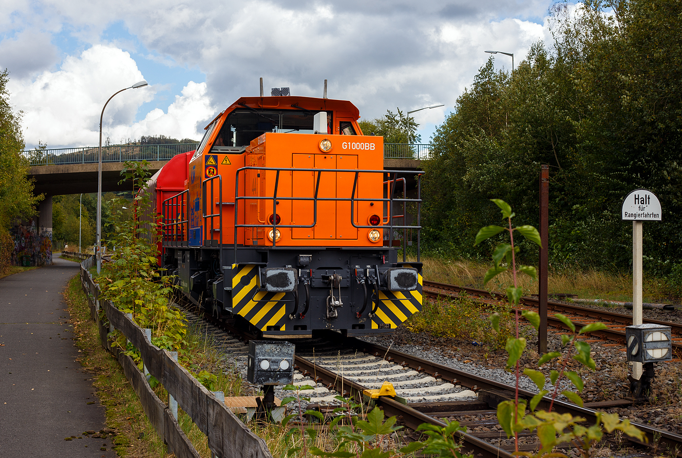 Die KSW 44 (92 80 1271 004-4 D-KSW) eine MaK G 1000 BB der KSW (Kreisbahn Siegen-Wittgenstein), steht am 12 September 2024 mit einem Übergabezug (leere Wagen), auf ihren Rangierbahnhof in Herdorf der Betriebsstätte FGE -Freien Grunder Eisenbahn (KSW NE447 / DB-Nr. 9275), vor der geschlossenen Gleisspeere, zur Abfahrt bereit. Aber noch muss sie den Gegenverkehr abwarten, bevor sie in Richtung Betzdorf losfahren kann. Rechts die DB-Strecke „Hellertalbahn“ (KBS 462) Betzdorf – Herdorf – Haiger.

Die Lok 44 wurde 2003 unter der Fabriknummer 1001462 bei Vossloh gebaut und am 05.01.2004 an die SK - Siegener Kreisbahn GmbH geliefert, welche ab Ende 2004 nun als Kreisbahn Siegen-Wittgenstein (KSW) firmiert.

Die G 1000 ist eine vierachsige dieselhydraulische Lokomotive für den schweren Rangier- und leichten Streckendienst. Die zuverlässige Vielzwecklokomotive ist mit modernster Technik ausgestattet und erfüllt daher die neuesten Vorschriften des Unfallschutzes. Die Anwendungsbreite der Lokomotive reicht vom leichten Rangierdienst in Einzeltraktion über den Einsatz als Streckenlokomotive in Mehrfachtraktion bis hin zum schweren Rangierdienst.

Mit der MaK G 1000 BB wird seit dem Jahr 2002 eine Lok für den Leistungsbereich unterhalb der G 1206 angeboten. Sie basiert auf der G 800 BB, von der außer dem kompletten Fahrwerk und Rahmen auch das Führerhaus und der hintere Vorbau übernommen wurden. Deutlich anders ist dagegen der vordere Vorbau, in dem Platz für den größeren Dieselmotor geschaffen wurde.

TECHNISCHE DATEN:
Spurweite: 1435 mm (Normalspur)
Achsfolge: B´B´
Länge über Puffer: 14.130 mm
Drehzapfenabstand: 6.700 mm
Radsatzabstand im Drehgestell: 2.400 mm
Treibraddurchmesser: 1.000 mm (neu) / 920 mm (abgenutzt)
größte Breite: 3.080 mm
größte Höhe über Schienenoberkante: 4.225 mm
Dienstgewicht: 80 t

Motorhauptdaten:
Motorbauart: MTU 90° V-8-Zylinder-Dieselmotor mit Common-Rail-Einspritzsystem, Abgasturbolader und Ladeluftkühlung
Motortyp: MTU 8V 4000 R41L
Leistung: 1.100 kW (1.475 PS) bei 1.860 U/min
Bohrung/Hub: 165/190 mm
Hubraum: 32,5l
Länge: 1.915 mm
Breite: 1.380 mm
Höhe: 1.800 mm
Gewicht (trocken): 4.700 kg

Anfahrzugkraft bei 20 t Achslast: 259 kN
Höchstgeschwindigkeit: 100 km/h  
Strömungsgetriebe: Voith L4r4
kleinster befahrbarer Gleisbogen: 80 m
Bremse: KE GP mZ (D)
Bremsgewichte: G/P: 65 t/96 t
Kraftstoffvorrat: 3000 l
