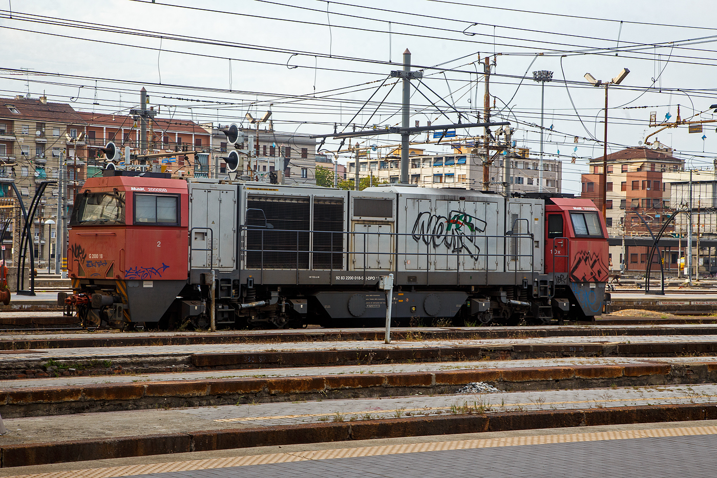 Die MaK G 2000 BB (eigentlich Vossloh G 2000-2 BB), die G 2000 18 ER (92 83 2200 017-5 I-DPO) der DP - Dinazzano Po S.p.A. (Reggio Emilia) ist am 23.07.2022 beim Bahnhof Milano Centrale abgestellt, 

Die G 2000-2 BB in der Variante der G 2000 BB mit breitem Führerhaus und links für Italien angeordnetem Führertisch wurde 2003 von Vossloh in Kiel unter der Fabriknummer 1001451 gebaut und als 
G 2000-005 an die ACT - Azienda Consorziale Trasporti (Reggio Emilia – Italien) ausgeliefert. Von 2009 bis 2012 war sie als G 2000 18 ER der FER - Ferrovie Emilia Romagna S.r.l. (Bologna) unterwegs.

Die Lokomotive Vossloh G 2000 BB ist die stärkste dieselhydraulische Lokomotive der Vossloh Locomotives GmbH und wird seit dem Jahr 2000 gebaut. Ihre Achsfolge ist B’B’. Sie hat eine Leistung von bis zu 2.700 kW und erreicht je nach Motorisierung eine maximale Geschwindigkeit von bis zu 140 km/h. Je nach Ausrüstungsvariante bringt sie es auf ein Dienstgewicht von 84 t bis 90 t. Dabei erreicht sie eine Anfahrzugkraft von 283 kN bei 87,3 t. Das Tankvolumen beträgt 5000 l. Insgesamt gibt es 99 Loks der Typen 1–3 und je eine Lok der Typen 4 und 5. 

War das breitere Führerhaus zunächst nur für die italienische Ausführung wegen des dort vorgeschriebenen Beimannes und der dort üblichen Linkssteuerung gedacht, wurde es auch bei der dritten Version für den Verkehr in Deutschland, Niederlande, Belgien und Frankreich beibehalten, allerdings mit Steuerplatz auf der rechten Seite. Bei der ersten Serie befindet sich der Steuerplatz in der Mitte.

Die Lokomotiven haben einen tragenden Rahmen mit angesetzten Frontschilden als Kollisionsschutz. An beiden Seiten gibt es einen Endführerstand, entweder asymmetrisch, mit einem leicht gewendelten Einstieg (Typ 1) oder (wie hier) über die ganze Fahrzeugbreite. Zum Ende ist der Führerraum leicht eingezogen, auch ab Fensterunterkante wird er nach oben etwas schmaler. Der Zugang zum Führerstand erfolgt von hinten über den Umlauf. Der modular aufgebaute Maschinenraum geht nicht über die ganze Breite, so dass auf beiden Seiten Platz für einen Umlauf mit Geländer gibt. Es gibt fünf Module: Elektronik und Batterien, Kühlanlage mit seitlichen Kühlblöcken, Verbrennungsluftfilter (über dem Getriebe), Motor mit Abgasschalldämpfer und die Druckluftanlage. Im Bereich der beiden Kühlertürme sind an der Seite und im Dach große Lüftungsgitter, unterm Dach mit Lüftungsrotoren. Die Lok hält das niedrige Umgrenzungsprofil UIC 505-1 ein. Als Drehgestelle werden zweiachsige Flexicoil-Drehgestelle mit Radsatzlenkern verwendet, wie sie auch in den anderen Typen der „vierten Generation“ von Vossloh verwendet werden. Als Motor kommt in der Regel ein Viertakt-Motor Caterpillar 3616 B-HD mit 2.240 kW zum Einsatz. Aufgrund der hohen Leistung ist ein Einbau eines Turbowendegetriebes nicht möglich, so kommt ein hydraulisches Voith-Getriebe L 620 reU2 mit nachgeschaltetem mechanischen Wendegetriebe zum Einsatz, das nur im Stillstand betätigt werden kann.

TECHNISCHE DATEN:
Achsformel: B'B'
Spurweite: 1.435 mm (Normalspur)
Länge über Puffer: 17.400 mm
Drehzapfenabstand: 9.500 mm
Achsstand im Drehgestell: 2.400 mm
Treibraddurchmesser:  1.000 mm
Höhe: 4.220 mm
Breite: 3.080 mm
Dieselmotor: Caterpillar V-16-Viertakt-Dieselmotor mit Turboaufladung und Ladeluftkühlung vom Typ CAD 3516 B-HD
Motorleistung: 2.240 kW
Motor-Nenndrehzahl:  1800/min
Getriebe: Voith L 620 reU2
Leistungsübertragung: hydraulisch
Anfahrzugkraft:  283 kN
Dienstgewicht: 87,3 t
Höchstgeschwindigkeit: 120 km/h
Kleinster bef. Halbmesser: 80 m
Bremse: KE-GP
Tankinhalt: 5.000 l
