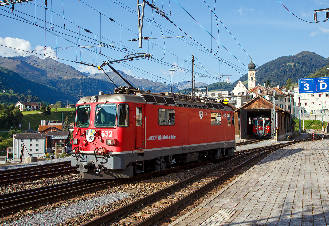 Die RhB Ge 4/4 II 632 „Zizers“ am 07 September 2021 beim Umsetzen im Bahnhof Disentis/Mustér. Zuvor hatte sie unseren Zug den RE 1721 von Chur nach hier gezogen. In Disentis/Mustér endet das Netz der Rhätischen Bahn (RhB), so setzt sich die Lok nun, für die Rückfahrt, ans andere Ende des Zuges.

Hier in Disentis/Mustér endet das Netz der RhB, aber hier beginnt, mit direktem Anschluss, das Netz der Matterhorn-Gotthard-Bahn (MGB) bzw. bis zur Fusion (zum 01. Jan. 2003) der eigenständigen Furka-Oberalp-Bahn (FO). 

Bei den durchgängigen geneinsamen Zügen dem berühmten Glacier-Express, findet in Disentis/Mustér ein Lokwechsel, zwischen RhB und MGB, stand. Die RhB ist eine reine meterspurige Adhäsionsbahn im Gegensatz die MGB ist eine meterspurige Bahn mit gemischtem Adhäsions- und Zahnradbetrieb.

Hinten in der Remise steht ein MGB Gepäcktriebwagen Deh 4/4 I, ex FO Deh 4/4 I, welche Fahrzeugnummer (51 bis 55) es ist kann in nicht sagen, da die Nummern an den Fronten nicht angeschrieben werden.