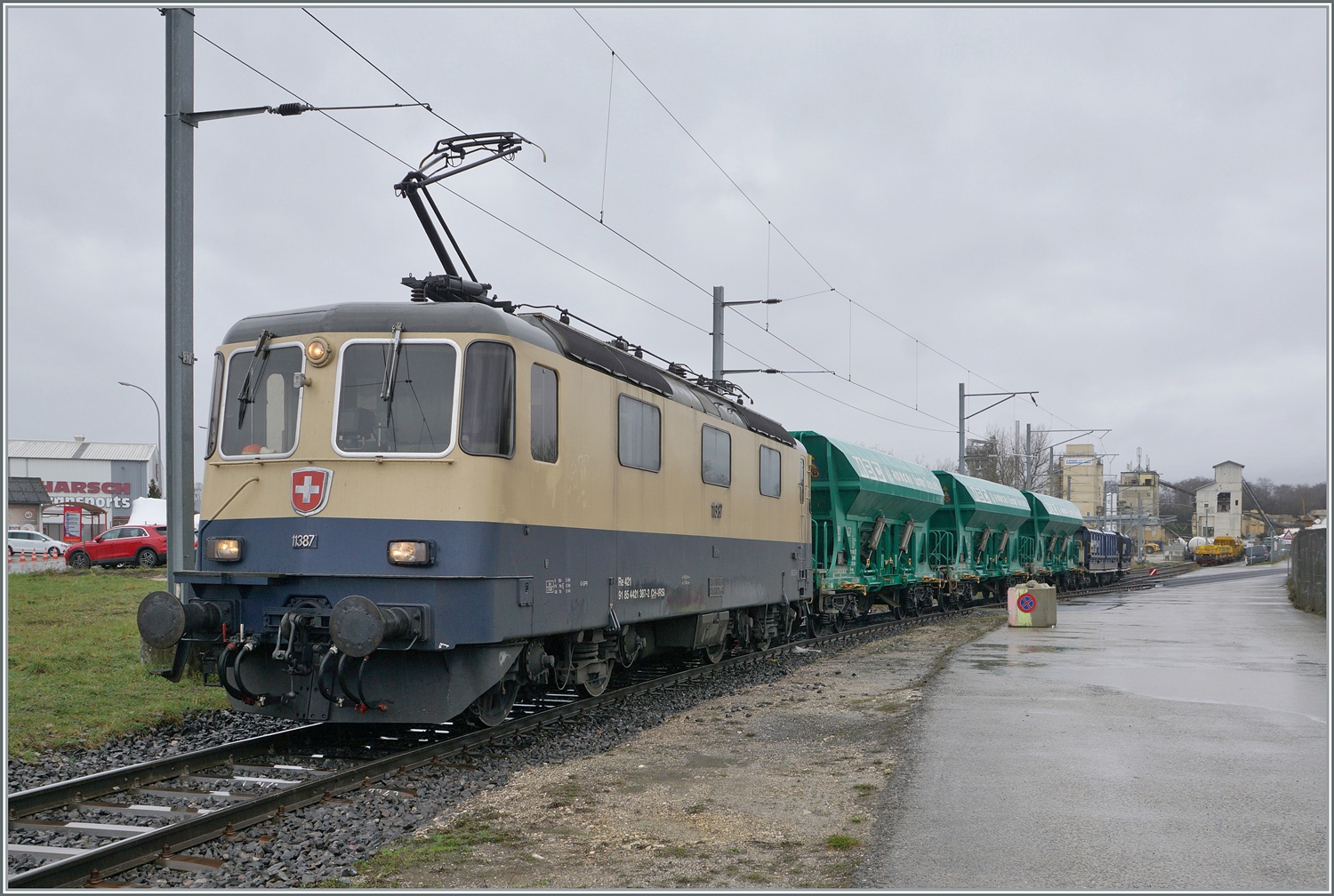 Etliche Regentropfen sp�ter kommt die IRSI/IGE  Rheingold  Re 4/4 II 11387 (Re 421 387-2) nun mi ihrem G�terzug nach Apples am Haken wieder aus dem Industrie Gel�nde bei Gland angefahren.

22. Februar 2024