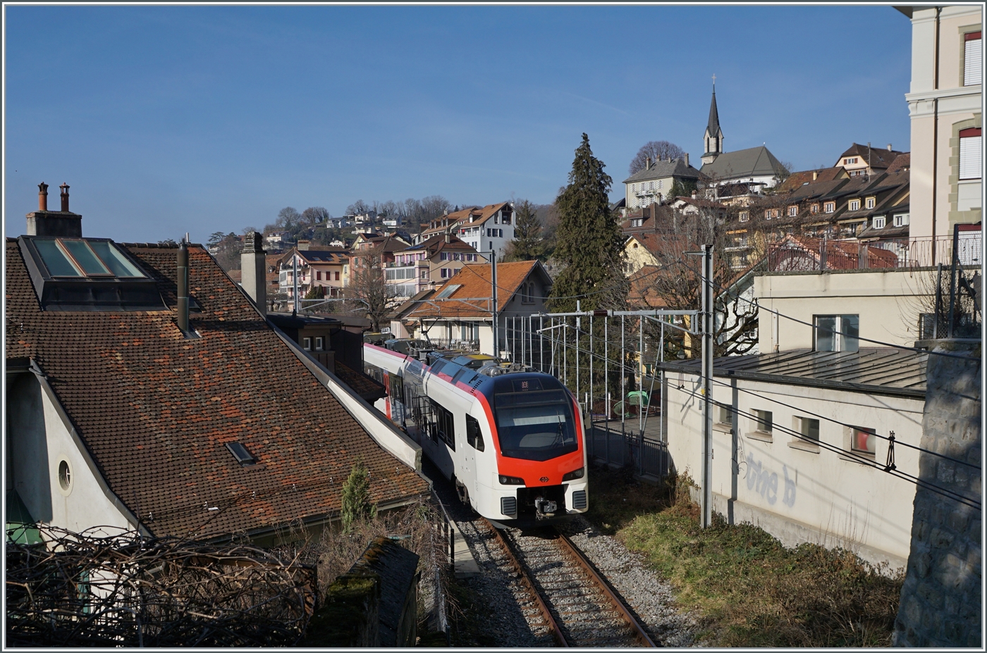 Fernverkehr  auf der Train de Vignes Strecke: der für den Fernverkehr beschaffte SBB Flirt3 RABe 523 503  Mouette  (RABe 94 85 0 523 503-6 CH-SBB) ist als S7 auf der Train de Vignes Strecke zwischen Puidoux und Vevey unterwegs und fährt gerade durch die eng aneinander gereihten Häuser von Chexbres.

11. Februar 2023