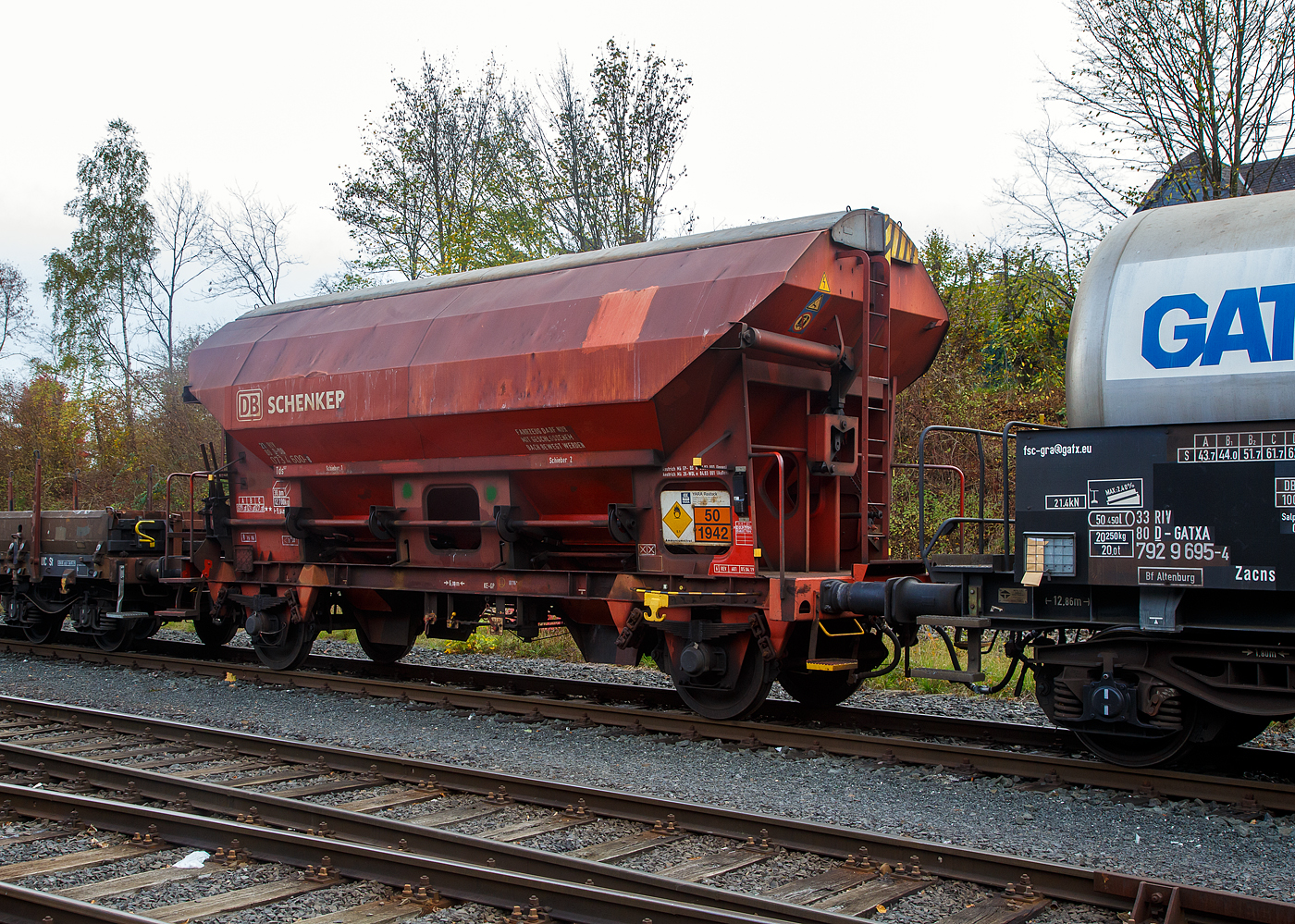 Gedeckter Schüttgutwagen mit dosierbarer Schwerkraftentladung und zwei Radsätzen 21 80 0734 600-8 D-DB, der Gattung Tds 937, der DB Cargo AG abgestellt, im Zugverband eines Übergabezuges der KSW, am 03.11.2022 in Herdorf auf dem Rbf. der KSW.

In diesen Wagen wird Ammoniumnitrat (Gefahrgutnummer 50/1942) zur Sprengstoff Herstellung zur Fa. Dynamit Nobel Defence nach Burbach-Würgendorf gefahren (hier ist er leer).  Ammoniumnitrat ist der Stoff  von dem ca. 2.750 Tonnen im Hafen von Beirut am 4. August 2020 explodierten und zur der bekannten gewaltigen Explosionskatastrophe führten.

Der Wagen trägt außerdem einen Aufkleber der Firma YARA Rostock, das zum norwegischen Konzern Yara International gehört. Yara ist ein Hersteller und Anbieter von Chemikalien und Industriegasen wie Dünger, Harnstoff, Nitraten und Ammoniak. Das Unternehmen entstand 2004 durch Abtrennung vom Unternehmen Hydro Agri, einem Firmenbereich von Norsk Hydro.

Die Wagen besitzen eine gleisseitige, dosierbare Entladeeinrichtung. Ein Innenanstrich erhöht bei den meisten der Fahrzeuge den Gebrauchswert, insbesondere durch den Schutz vor Verunreinigungen, Möglichkeiten des Transportes von Lebensmitteln, günstigeres Entladeverhalten (Rutschverhalten) bei schwer fließenden Gütern sowie durch verbesserten Korrosionsschutz bei aggressiven Ladegütern.

Der Wagen ist für den Transport von nässeempfindlichen Schüttgütern aller Art, wie z. B. Salze und Düngemittel, vorgesehen. Sie besitzen eine gleisseitige, dosierbare Entladeeinrichtung. Ein Innenanstrich erhöht bei den meisten der Fahrzeuge den Gebrauchswert, insbesondere durch den Schutz vor Verunreinigungen, Möglichkeiten des Transportes von Lebensmitteln, günstigeres Entladeverhalten (Rutschverhalten) bei schwer fließenden Gütern sowie durch verbesserten Korrosionsschutz bei aggressiven Ladegütern. Der Transport grobkörniger oder kantiger, schwerer Güter (z. B. Kies, Schlacke, Schotter) ist wegen einer möglichen Beschädigung der Innenbeschichtung nicht zulässig.

Das Untergestell und der Wagenkasten sind als Schweißkonstruktion unter Verwendung von Walzprofilen und Blechen hergestellt. Beide Teile sind miteinander verschweißt. Der Wagen besitzt zwei Bühnen, die von beiden Seiten zugänglich sind. Beide Bühnen sind mit einer Sprossenleiter versehen. Die Arbeitsbühne ist mit Handhebeln zur Betätigung der Wölbschieber, mit dem Handrad zur Öffnung des Daches und teilweise mit einer Feststellbremse und Notbremshahn ausgerüstet. Der Neigungsgrad des trichterförmigen Wagenkastens ermöglicht eine restlose selbsttätige Entladung. Die Entladung des Wagens erfolgt über Wölbschieber. Der Wagen ist mit einem einschaligen Hubschwenkdach ausgerüstet. Das Dach wird vor dem Schwenken angehoben und dann seitlich abgeschwenkt, wobei die gesamte Breite der Beladeöffnung freigegeben wird. Im geschlossenen Zustand ist das Dach gegen unbeabsichtigtes Verschwenken gesichert.

TECHNISCHE DATEN:
Spurweite: 1.435 mm
Achsanzahl: 2
Länge über Puffer: 9.640 mm
Achsabstand: 6.000 mm
Laufraddurchmesser: 1.000 mm (neu)
Wagenhöhe: 4.198mm
Größe der Beladeöffnung Länge x Breite: 8.000 x 1.200 mm
Laderaum: 38 m³
Eigengewicht: 12.700 kg
Höchstgeschwindigkeit: 100 km/h (beladen) / 120 km/h (leer)
Maximales Ladegewicht: 27,0 t  ab Streckenklasse C
Kleinster bef. Gleisbogenradius: 35 m
Bauart der Bremse: KE-GP (LL)
Bremssohle: IB 116
Intern. Verwendungsfähigkeit: RIV

Auch in dem Kesselwagen davor 33 80 7929 695-4 D-GATXD, der Gattung Zacns, wurde ein Rohstoff für die Herstellung von Sprengstoffen transportiert und zwar Salpetersäure.