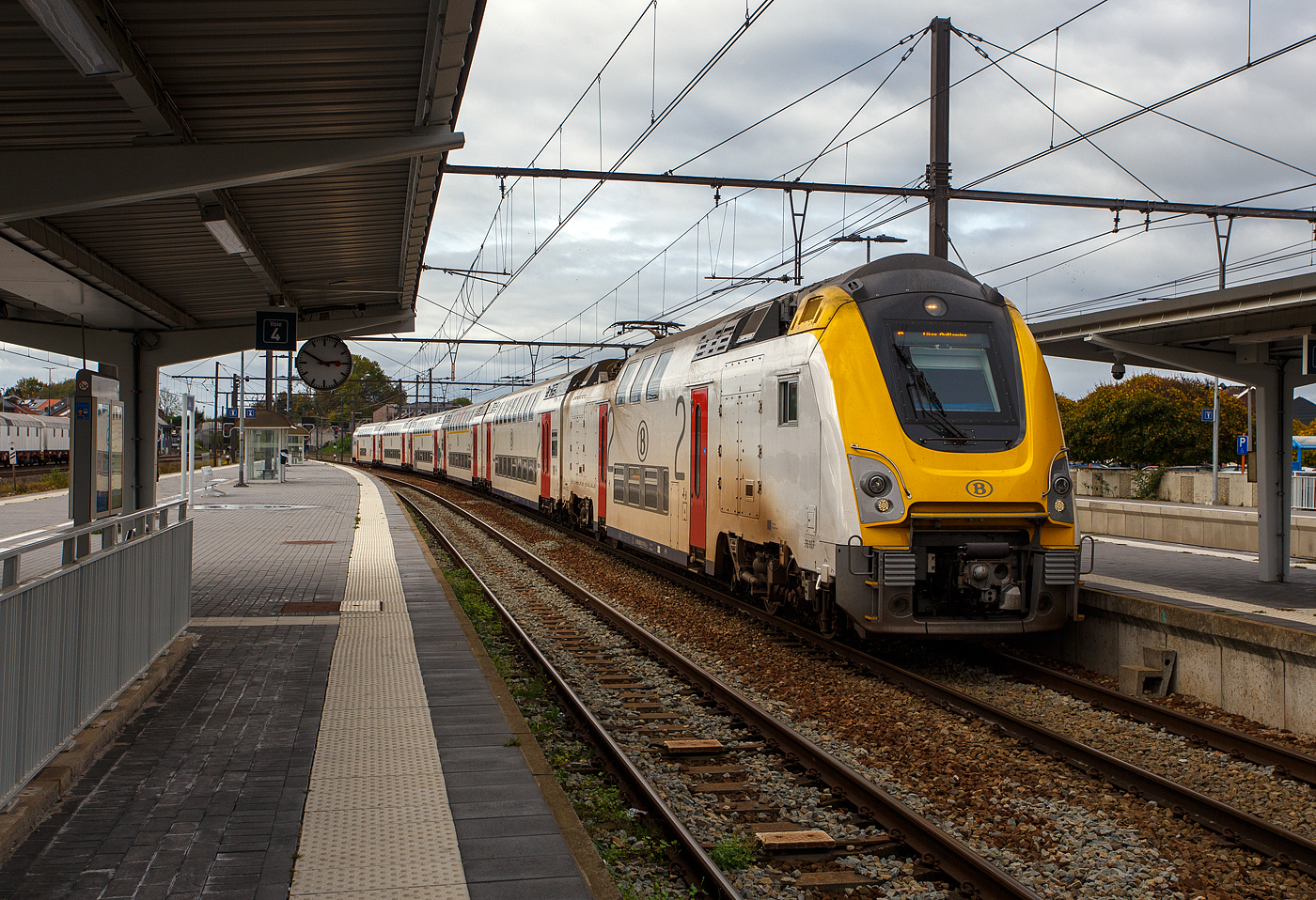 Gef�hrt von dem SNCB/NMBS - M7 Bmx TWINDEXX-Triebwagen 91 88 8696 10 7-0 B-B, ex 76107, erreicht der IC 2811 von Knokke �ber Gent und Br�ssel nach L�ttich/Li�ge-Guillemins, am 21 Oktober 2025 den Bahnhof Ans. 

Von diesen Triebwagen wurden 116 St�ck ab 2020 von Alstom/ACEC, 65 St�ck davon im Alstom-Werk in Valenciennes, die �brigen 51 Triebwagen wurden im nun auch zum franz�sischen Alstom S.A. Konzern geh�renden ehemaligen BN-Werk in Br�gge produziert. Die elektrische Ausr�stung ist von ACEC - Ateliers de constructions �lectriques de Charleroi (Alstom Belgium). 

Von den M7 Doppelstock-TWINDEXX-Wagen wurden bereits ab 2018 �ber 530 St�ck von Bombardier Transportation, ab Januar 2021 vom franz�sischen Alstom Konzern �bernommen, gebaut. Die Wagen kommen auch in Lok bespannten Z�gen (u.a. Serie HLE 18/19 / SIEMENS EuroSprinter ES60U3) zum Einsatz. Die M7-Wagen basieren auf den bekannten M6-Wagen der Twindexx-Plattform (von Bombardier), jedoch gibt es erstmals auch Triebwagen, sodass auch Triebwagenz�ge ohne zus�tzliche Lokomotive gebildet werden k�nnen. Geplant ist ein Einsatz der M7-Wagen in Belgien, den Niederlanden und Luxemburg.

Die ersten M7-Wagen nahmen im Januar 2020 den kommerziellen Betrieb auf. Die ersten drei Wagen wurden mit M4-Wagen in P-Z�gen zwischen L�ttich-Guillemins und Br�ssel-Midi eingesetzt, anschlie�end mit I11-Wagen in P-Z�gen zwischen Vis�, L�ttich und Br�ssel-Midi �ber die Hochgeschwindigkeitsstrecke LGV 2.

Design und Technik:
Bestellt wurden von der SNCB (Soci�t� nationale des chemins de fer belges) / NMBS (Nationale Maatschappij der Belgische Spoorwegen) folgende Varianten der M7-Wagen, die mit unterschiedlichen Gattungsbuchstaben gekennzeichnet sind:
•	AB bezeichnet gemischtklassige Mittelwagen erster und zweiter Wagenklasse mit 58 Pl�tzen in der 1. Klasse und 75 Pl�tzen in der 2. Klasse.
•	B bezeichnet Mittelwagen zweiter Wagenklasse mit 140 Pl�tzen in der 2. Klasse.
•	BDx bezeichnet Steuerwagen zweiter Wagenklasse mit Mehrzweckabteil und Anpassung f�r Menschen mit Behinderung, mit Bahnsteigh�he von 630 mm mit 100 Pl�tze in der 2. Klasse
•	BD bezeichnet Mittelwagen zweiter Wagenklasse mit Mehrzweckabteil und Anpassung f�r Menschen mit Behinderung, mit Bahnsteigh�he von 760 mm.
•	Bx bezeichnet Steuerwagen zweiter Wagenklasse mit Anpassung f�r Menschen mit Behinderung, mit Bahnsteigh�he von 760 mm mit 102 Pl�tzen in der 2. Klasse.
•	Bmx bezeichnet die Triebwagen mit 52 Pl�tzen der 2. Klasse und F�hrerstand.

Der Wagenkasten ist eine selbsttragende, modulare Stahlkonstruktion. Der Oberboden besteht aus stranggepresstem Aluminiumprofilen mit Schalld�mmung und Holzpaneelen. Die Front der Trieb- und Steuerwagen besteht aus glasfaserverst�rktem Kunststoff und bildet eine Schale, die die Metallstruktur umschlie�t und den Fahrer vor St��en sch�tzt. Die Wagenbremsen verf�gen �ber sechs Scheibenbremsen und elektromagnetische Bremsbel�ge, die f�r eine Geschwindigkeit von 200 km/h erforderlich sind. Neben der automatischen und magnetischen Bremse k�nnen die M7 auch elektrodynamisch bremsen, und die nicht angetriebenen Wagen sind mit einer Spindelbremse ausgestattet. Auf den D�chern befinden sich eine Klimaanlage und ein statischer Umformer. Die Wagen verf�gen �ber Luftbeh�lter f�r Bremsen und Magnetbremsen sowie f�r die T�rsteuerung und die Drehgestell-Luftfederung. 

M7 Bmx Triebwagen:
Die Einf�hrung von Dreispannungs- Doppelst�ckigen-Triebwagen (3 kV und 1,5 kV DC, sowie25 kV 50 Hz AC) ist f�r die SNCB eine Premiere. Diese Bauweise bietet im Vergleich zu einem gezogenen Zug den Vorteil, dass die gesamte Nutzl�nge der Bahnsteige f�r den Fahrgasteinstieg genutzt werden kann. Gleichzeitig bleibt die M�glichkeit bestehen, die Zugzusammensetzung je nach Bedarf zu �ndern, sei es tags�ber auf derselben Strecke, wodurch die Zusammensetzung in den Spitzenzeiten verst�rkt wird, oder langfristig. 

Die als Bmx bezeichnet Triebwagen mit 52 Sitzl�tzen in der 2. Klasse und einem F�hrerstand, k�nnen sowohl im konventionellen, mit 1,5 kV/3 kV Gleichspannung elektrifizierten Bestandsnetz, als auch auf Schnellfahrstrecken, die mit 25 kV Wechselspannung bei 50 Hz versorgt werden, verkehren. Als Zugbeeinflussungssystem wird ETCS Level 2 verwendet. Die Z�ge haben auch TBL1+ erhalten. Die Triebwagen verf�gen je L�ngsseite jeweils �ber zwei einfl�glige T�ren mit einer lichten Weite (Durchgang) von 1.030 mm. In den Triebwagen wie auch den Steuerwagentypen f�hrt auf der F�hrerstandsseite eine Treppe mit Podest zum Oberdeck.

Ein Drittel des Triebwagens ist mit Sitzpl�tzen ausgestattet. Dieses Fahrzeug verf�gt nicht �ber eine Toilette, aber ein Gang f�hrt durch den hinteren Maschinenraum zum n�chsten Wagen. Wegen dem Maschinenraum haben die Triebwagen nur eine Treppe zum Oberdeck, das durch eine automatische L�rmschutzt�re zug�nglich ist.

Der Triebwagen verf�gt nur �ber vier Scheibenbremsen, und das Leistungsgewicht begrenzt seine Geschwindigkeit im Alleinbetrieb ohne Personenwagen auf 100 km/h. Die Triebwagendrehgestelle und die Au�enachse des Steuerwagendrehgestells sind mit einem Schmiernippel ausgestattet, der den Radverschlei� im Betrieb reduziert. Der Triebwagen verf�gt neben seinem Motor auch �ber zwei Kompressoren zur Versorgung der Brems- und Zugsysteme sowie einen Hilfskompressor zum Anheben der Stromabnehmer (ein Stromabnehmer f�r Gleichstrom und einer f�r Wechselstrom). Der Umformer des Triebwagens nimmt einen Teil des Stroms aus der Oberleitung auf und wandelt ihn in 24 V Gleichstrom (Beleuchtung, Batterien), 400 V Drehstrom (Klimaanlage) und 230 V Wechselstrom (Steckdosen f�r Fahrg�ste) um.

Motorisierung:
Die von Alstom Le Creusot (Frankreich) hergestellten Triebdrehgestelle sind mit jeweils zwei Fahrmotoren ausgestattet, die mit Drehstrom betrieben und von einem Wechselrichter gespeist werden (einer pro Fahrmotor). Die Triebwagen sind f�r den Betrieb mit 3 kV Gleichstrom, 25 kV 50 Hz und 1,5 kV Gleichstrom ausgelegt und liefern eine Leistung von 3.000 kW. Diese kann vor�bergehend auf 3.300 kW erh�ht werden, wenn die Bedingungen f�r die Aktivierung des „Boost“-Modus erf�llt sind. In diesem Fall entwickelt das Antriebssystem jeder Achse 825 kW statt 750 kW.

TECHNISCHE DATEN des Bmx Triebwagen:
Spurweite: 1.435 mm (Normalspur)
Achsfolge: Bo'Bo'
L�nge �ber Puffer: 24.190 mm
Drehzapfenabstand:16.190 mm
Achsstand im Drehgestell: 2.650 mm
Treibraddurchmesser: 1.010 mm (neu)
Wagenkastenbreite: 2.830 mm
H�he: 4.630 mm (ohne Stromabnehmer)
Eigengewicht: 81 t
H�chstgeschwindigkeit: 200 km/h (bei 3 kV DC und 25 kV AC) / 150 km/h (1,5 kV DC) / 100 km/h (Triebwagen alleine, ohne Wagen)
Traktionskontrolle: 4 St�ck IGBT-Wechselrichter (Der Wechselrichter erm�glicht den Einsatz der dynamischen Bremse)
Motoren: 4 St�ck Drehstrommotore (3-Phasen-Wechselstrommotore)
Traktionsleistung am Rad: 4 x 750 kW = 3.000 kW (mit Boost kurzzeitig 3.300 kW)
Max. Leistung Widerstandsbremse: 2.400 kW
Max. Leistung Nutzbremse/Rekuperationsbremse: 3.000 kW
Anzahl der Stromabnehmer: 2
Stromsystem: 3 kV und 1,5 kV Gleichstrom, sowie 25 kV 50 Hz Wechselstrom
Sitzpl�tze: 52 in der 2. Klasse

Die M7-Wagen:
Durch Bedenken hinsichtlich der Barrierefreiheit, der Einstiegsh�he von 630 mm f�r Menschen mit eingeschr�nkter Mobilit�t zug�nglichen T�ren liegt unter der Standardbahnsteigh�he von 760 mm. Diese Kritik f�hrte zur Bestellung zweier Typen von Wagen mit unterschiedlichen Einstiegsh�he 630 mm und 760 klpmm, bei den Steuerwagen sowie bei dem Mittelwagen. 

Steuerwagen M7 BDx bzw. M7 BVx:
Als BDx werden die Steuerwagen zweiter Wagenklasse mit Mehrzweckabteil und Anpassung f�r Menschen mit Behinderung, mit Bahnsteigh�he von 630 mm, mit 100 Sitzpl�tze in der 2. Klasse, bezeichnet. Der Steuerwagen verf�gt im Unterdeck �ber ein Mehrzweckabteil mit quer angeordneten Klappsitzen und Rollstuhlpl�tzen, sowie einer Toilette mit Wickeltisch.
Als BVx werden die Steuerwagen zweiter Wagenklasse mit Anpassung f�r Menschen mit Behinderung, mit Bahnsteigh�he von 760 mm mit 102 Sitzpl�tzen in der 2. Klasse, bezeichnet. Der Steuerwagen BVx unterscheidet sich, neben der Einstiegh�he, vom Steuerwagen BDx durch das Fehlen einer Toilette, einen gr��eren Fahrradbereich und mehr Klappsitze.
Beide Typen verf�gen je L�ngsseite jeweils �ber eine einfl�glige T�r mit einer lichten Weite (Durchgang) von 1.030 mm, sowie einer zweifl�gligen T�r mit einer lichten Weite (Durchgang) von 1.710 mm.

TECHNISCHE DATEN der Steuerwagen:
Spurweite: 1.435 mm (Normalspur)
Achsfolge: 2'2' (4 Achsen)
L�nge �ber Puffer: 27.200 mm
Drehzapfenabstand: 20.000 mm
Achsstand im Drehgestell: 2.500 mm
Laufraddurchmesser: 1.010 mm (neu)
Wagenkastenbreite: 2.830 mm
H�he: 4.630 mm
Eigengewicht: 56 t
H�chstgeschwindigkeit: 200 km/h
Sitzpl�tze: 100 bzw. 102 in der 2. Klasse

Die Mittelwagen M7 AB, M7 B und M7 BD:
Als AB werden die 1./2. Klasse Mittelwagen (Doppelstock-Reisezugwagen) bezeichnet. Diese haben 58 Sitzpl�tzen in der 1. Klasse und 75 Sitzpl�tzen in der 2. Klasse, die Einstiegsh�he betr�gt 630 mm.
Als B werden die 2. Klasse Mittelwagen (Doppelstock-Reisezugwagen), mit einer Einstiegsh�he von 630 mm, bezeichnet. Die B-Wagen haben 140 Sitzpl�tzen in der 2. Klasse.
Als BD werden die 2. Klasse Mittelwagen (Doppelstock-Reisezugwagen) mit Mehrzweckabteil und Anpassung f�r Menschen mit Behinderung, mit Bahnsteigh�he (Einstiegsh�he) von 760 mm. Die BD-Wagen haben 130 Sitzpl�tzen in der 2. Klasse und Rollstuhlpl�tzen im Mehrzweckabteil, sowie eine rollstuhlgerechte Toilette.
Die AB und B Wagen verf�gen je L�ngsseite jeweils �ber 2 zweifl�glige T�ren, �ber dem Drehgestell, mit einer lichten Weite (Durchgang) von 1.710 mm. Die BD haben jeweils eine zweifl�glige T�r �ber dem Drehgestell und eine tiefere gesetzte einfl�gelige T�r mit stufenlosen Zugang bei Bahnsteigh�he von 760 mm.

TECHNISCHE DATEN der Steuerwagen:
Spurweite: 1.435 mm (Normalspur)
Achsfolge: 2'2' (4 Achsen)
L�nge �ber Puffer: 26.800 mm
Drehzapfenabstand: 20.000 mm
Achsstand im Drehgestell: 2.500 mm
Laufraddurchmesser: 1.010 mm (neu)
Wagenkastenbreite: 2.830 mm
H�he: 4.630 mm
Eigengewicht: 64 t (AB 63 t)
H�chstgeschwindigkeit: 200 km/h
Sitzpl�tze: s.o.

Quellen: Wikipedia (Deutsch und Franz�sisch), mmfl58.be und Anschriften 
Stand: Oktober 2025
