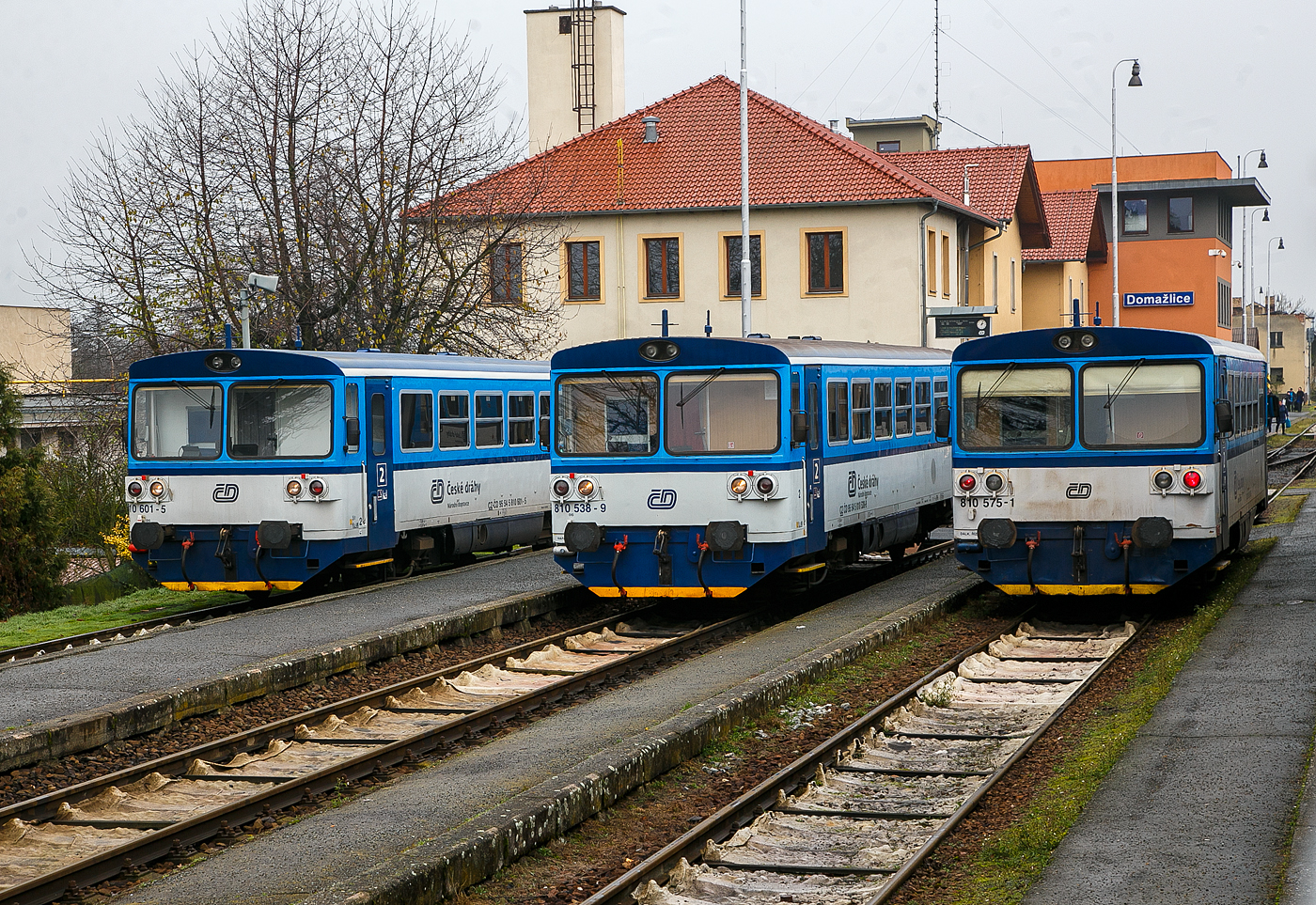 Gleich drei Brotb�chsen...
Die drei zur „RegioMouse“ modernisierte “Chc�p�k”  (Brotb�chsen), zweiachsige Dieseltriebwagen der ČD BR 810 (ex ČSD M 152.0) stehen am 22.11.2022 im Bahnhof Doma�lice (Taus) zur Abfahrt bereit. Es sind von links nach rechts, der (CZ-ČD 95 54 5) 810 601-5, 810 538-9 und 810 575-1. 

Die zweiachsige Dieseltriebwagen f�r den Regionalverkehr wurden als Baureihen M 152.0 (ab 1988: Baureihe 810) f�r die Tschechoslowakischen Staatsbahnen (ČSD) gebaut. Die Fahrzeuge bilden die dritte Generation zweiachsiger Triebwagen der ČSD. Die seit 2018 einer zweiten Modernisierung unterzogenen Fahrzeuge der ČD-Baureihen 809 und 810 werden als „RegioMouse“ vermarktet.

Ab 1975 wurden bei Vagonka Tatra in Stud�nka (heute �koda Vagonka a.s.) in sieben Bauserien 680 zweiachsige Dieseltriebwagen f�r die ČSD als Baureihe M 152.0 gebaut. Nahezu baugleiche Fahrzeuge wurden an die Ungarischen Staatsbahnen (M�V), als Bzmot, geliefert. Passend zu den Triebwagen wurden entsprechende Beiwagen vom Typ Blm geliefert, welche in Aufbau und Aussehen identisch mit den Triebwagen sind. Jedem Triebwagen konnten zwei Beiwagen beigegeben werden. Aufgrund der eckigen Aufbauten erhielten die Triebwagen von deutschen Eisenbahnfreunden den Spitznamen „Brotb�chse“.

Zwischen 1987 und 1990 f�hrten die ČSD EDV-gerechte Triebfahrzeugnummern ein. In der �bergangszeit wurden die EDV-Nummern zus�tzlich zu den alten Gussschildern mit Klebeziffern angebracht. Die Triebwagen erhielten die Reihenbezeichnung 810, die Beiwagen 010. Beide Nachfolgeunternehmen der ČSD behielten den Nummernplan bei, allerdings wurden freiz�gig einsetzbare Beiwagen 2009 auch nummernm��ig in den Reisezugwagenpark aufgenommen.

Nach der Teilung der Tschechoslowakei in die Nachfolgestaaten Tschechien und Slowakei am 1. Januar 1993 wurden Trieb- und Beiwagen auf die neugegr�ndeten Staatsbahnen ČD und �SR aufgeteilt. In der Slowakei geh�ren die Fahrzeuge heute zum Bestand des Nachfolgeunternehmens �elezničn� spoločnosť Slovensko (ZSSK).

Technische Merkmale:
Die Triebwagen haben keine Vielfachsteuerung, passende Steuerwagen existieren nicht. Deshalb muss bei mehrteiligen Einheiten jeder Triebwagen mit einem Triebfahrzeugf�hrer besetzt sein. Die Triebwagen m�ssen, wenn sie mit entsprechenden Beiwagen verkehren,  an Endbahnh�fen stets an die jeweilige Zugspitze umgesetzt werden.

Aufbau des Triebwagens:
Der Triebwagen ist eine Leichtbaukonstruktion. Der Wagenkasten besteht aus gewalzten und abgekanteten Stahlprofilen, die mit Stahlblech verkleidet sind. Innen ist das Gerippe mit Spanplatten, die mit Sprelacart �berzogen sind, verkleidet. Der Fu�boden besteht aus wasserbest�ndigem Sperrholz von 15 Millimetern Dicke und ist mit einer zwei Millimeter starken Schicht aus PVC beklebt. An jedem Ende des Wagenkastens befindet sich ein vom F�hrerstand abgetrennter Einstiegsraum, der auf beiden Seiten jeweils eine vom F�hrerstand schlie�bare pneumatische Schiebet�r besitzt.

Das Fahrgastabteil besitzt 56 Sitzpl�tze in der Anordnung 3+2 mit Mittelgang, die urspr�nglich schaumgummigepolstert waren. Zus�tzlich bietet ein Wagen etwa 40 Stehpl�tze. Der Fahrgastraum hat auf jeder Seite sechs Fenster mit der lichten Weite von 1316 � 841 mm, deren oberer Teil klappbar ist. Gro�e Frontscheiben mit Scheibenheizung, Scheibenwischern und Sonnenschutzblende erm�glichen eine gute Streckenbeobachtung. Durch die Anordnung einer zus�tzlichen Trennwand fielen die F�hrerst�nde sehr kurz aus. Um eine befriedigende Sitzposition f�r den Triebwagenf�hrer zu erm�glichen, musste die Trennwand im Bereich seines Sitzes ausgeschnitten werden. Der Ausschnitt ist mit einer in den Einstiegsraum reichenden Blechabdeckung verschlossen.

Die Beiwagen entsprechen im Aufbau den Triebwagen, abgesehen von der fehlenden Antriebsanlage. An Stelle der F�hrerst�nde ist an den Wagenenden eine durchgehende Sitzbank vorhanden.

Laufwerk und Antriebsanlage:
Gef�hrt wird das Fahrzeug von zwei einachsigen Drehgestellen, von denen eines �ber eine Gelenkwelle angetrieben wird. Damit sind beide Rads�tze im Bogen radial einstellbar. Die Drehgestelle st�tzen sich mit Schraubenfeder auf den Achslagern ab. Die Aufh�ngungen sind mit dem Wagenkasten �ber Gummibl�cke verbunden. Auf der Treibachse, die beidseitig gesandet werden kann, sitzt das Wendegetriebe zur Umsteuerung der Fahrtrichtung. Bei den Triebwagen sind beide Rads�tze mit einer Spurkranzschmiereinrichtung ausger�stet.

Als Antriebsanlage ist ein nicht aufgeladener Dieselmotor vom Typ LIAZ ML 634 unterflur eingebaut. Dieser besitzt sechs Zylinder in Reihe mit Direkteinspritzung und ist mit dem Getriebe vom Typ Praga 2M 70 direkt verbunden. Die gesamte Antriebsanlage besteht bis auf das Achswendegetriebe aus Komponenten, die vom Omnibus Karosa �M 11 �bernommen wurden. 

Die Antriebsanlage und die Hilfseinrichtungen wie Wasserk�hlung, �lw�rmetauscher, Batterie, Kraftstoffbeh�lter und Warmwasserheizung sind unterflur angeordnet. Deshalb d�rfen die Triebwagen Ablaufberge nicht befahren. Die Hilfsmaschinen, ein Wechselstromgenerator und ein Kompressor f�r die Druckluft der pneumatischen Bremse, werden �ber Gelenkwelle und Keilriemen vom Dieselmotor angetrieben. Der Dieselmotor ist wassergek�hlt, zus�tzlich ist ein L�fter mit hydrostatischem Antrieb vorhanden. Dieser wird in Abh�ngigkeit von der Motordrehzahl und der K�hlwassertemperatur automatisch geregelt.

�brige Einrichtungen:
Die Triebwagen sind mit indirekter Bremse und direkter Bremse nach dem System DAKO ausger�stet. Gesteuert wird diese mit dem F�hrerbremsventil �koda N – 0. Au�erdem ist eine Handbremse, die in beiden F�hrerst�nden bedient werden kann, vorhanden. In beiden Einstiegsr�umen und dem Fahrgastraum befinden sich Notbremsh�hne.

Beheizt wird das Fahrgastabteil des Triebwagens durch Warmluft. Hierzu wird das K�hlwasser aus dem Motorkreislauf einem W�rmetauscher zugef�hrt, der unter den Sitzen angebracht ist. Bei nichtarbeitendem Dieselmotor wird ein Vorw�rmger�t verwendet. Der F�hrerstand wird mit einer Warmwasserheizung beheizt. Die Beiwagen werden elektrisch beheizt. Bel�ftet wird das Abteil der Reisenden �ber Dachl�fter. Die Beleuchtung des Fahrgastabteiles �bernimmt der Wechselstromgenerator. Durch die Ausr�stung der Trieb- und Beiwagen mit Seitenpuffern und Schraubenkupplung ist es m�glich, die Fahrzeuge mit anderen Fahrzeugen zu kuppeln. Daher k�nnen die Triebwagen vereinzelte G�tertransporte auf Nebenbahnen durchf�hren. Die Schraubenkupplungen entsprechen der bei Dieseltriebwagen der ČSD �blichen leichten Ausf�hrung, die damit ausger�steten Wagen d�rfen in Regelz�gen nur am Schluss eingestellt werden.

Umbauten in Tschechien  (der ČD): 
1994 begann der Umbau von 28 Einheiten f�r den schaffnerlosen Betrieb. Dabei wurde die Inneneinrichtung ge�ndert. 1996 wurden diese Einheiten in die ČD-Baureihe 809 umgezeichnet.

Von 2005 bis 2012 wurden die Fahrzeuge der ČD durch die Firma Pars Nova (geh�rt zu �koda) grundlegend modernisiert und umgebaut. Dabei entstanden zweiteilige Einheiten, die jeweils aus einem Triebwagen und einem teilweise niederflurigen Steuerwagen bestehen. Ein Teil der Triebz�ge wurde als dreiteilige Einheit mit zwei Triebwagen und einem dazwischen eingestellten Beiwagen zusammengestellt. Bei den Wagen, die einen zwischen den Rads�tzen abgesenkten Wagenboden erhielten, wurden die Einstiege von den Enden in Wagenmitte verlegt.

Im Februar 2018 wurde als letzte Modernisierung die Baureihe 816 von GW Train Regio vorgestellt.

Einsatz:
Die Fahrzeuge besitzen eine Zulassung f�r den Verkehr nach Deutschland und �sterreich. Im grenz�berschreitenden Nahverkehr geh�rten sie auf den Grenzbahnh�fen Zittau, Ebersbach (Sachs), Bad Schandau, Johanngeorgenstadt, Furth im Wald und Bayerisch Eisenstein zum t�glichen Bild. 

Trotz des Umbauprogrammes existieren nach wie vor einige Fahrzeuge, die sich bis auf eine Teilmodernisierung des Fahrgastraumes mit neuer Bestuhlung noch weitgehend im Originalzustand befinden. Sie kommen weiterhin auf Strecken mit geringem Verkehrsaufkommen planm��ig zum Einsatz. Bei den ČSD war es �blich, Beiwagen von Verbrennungsmotortriebwagen auch als lokbespannte Reisez�ge einzusetzen. Die Nachfolger behielten diese Betriebsweise bei.

TECHNISCHE DATEN :
Hersteller: ČKD Vag�nka in Stud�nka (heute �koda Vagonka a.s.)
Spurweite: 1.435 mm (Normalspur)
Achsformel: 1'A' 
L�nge �ber Puffer: 13.970 mm
H�he: 3.500 mm
Achsabstand: 8.000 mm
Dienstgewicht: 20 t
Radsatzfahrmasse: 10 t
H�chstgeschwindigkeit: 80 km/h
Installierte Leistung: 155 kW (bei 1.950 U/min)
Anfahrzugkraft: 29 kN 
Motorbauart: Sechszylinder-Reihendieselunterflurmotor
Motorentyp: LIAZ ML 634
Motorhubraum: 11,946 Liter (Zylinder-� 130 mm / Kolbenhub 150 mm)
Nenndrehzahl: 2.150 U/min (Leerlaufdrehzahl 600 U/min)
Kompressionsverh�ltnis: 12,5 : 1
Getriebe: Praga 2M70
Leistungs�bertragung: hydromechanisch
Sitzpl�tze: 55
Tankinhalt: 300 l
Fu�bodenh�he: 570 mm (Niederflurteil)
Kleinster befahrbarer Gleisbogen: R 100 m

Quellen: Wikipedia, atlaslokomotiv.net
