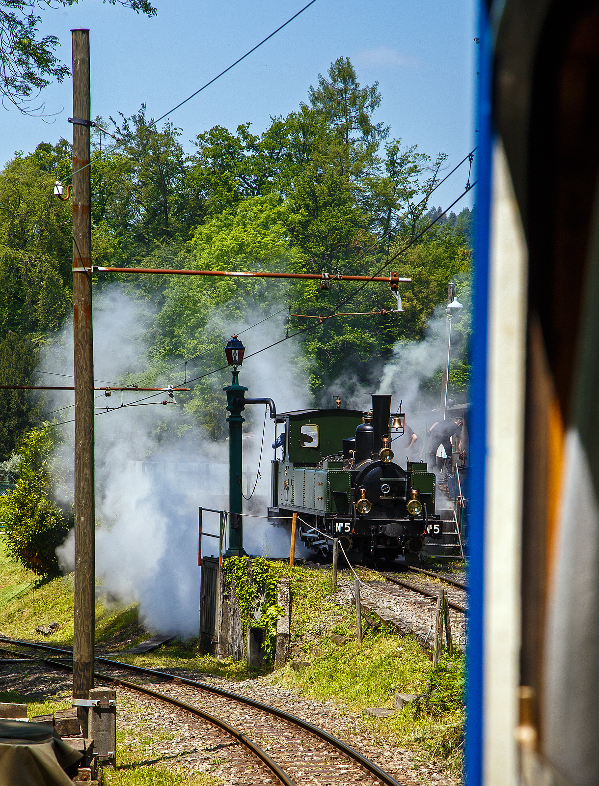 Museumsbahn-Romantik pur – Pfingsten 2023 (Samstag 27. bis Montag 29. Mai 2023) fand bei der Museumsbahn Blonay–Chamby das Schweizer Dampffestival 2023 / Festival suisse de la Vapeur 2023 statt.

Bei der Dampflok-Wartungsstelle der Museumsbahn Blonay–Chamby beim Museumsareal in Chaulin steht am 27.05. 2023 die G 3/3 LEB N° 5  Bercher  der Museumsbahn zum Kohlefassen. Links die Strecke 115 der MVR hinab nach Blonay, wir fahren mit dem ex MOB BCFe 4/4 11 rechts das Stichgleis zum Museum bzw. Depot hinauf.

Die ex LEB Nr. 5  Bercher  (Lausanne–Echallens–Bercher-Bahn) wurde 1890 von der Elsässische Maschinenbau-Gesellschaft Grafenstaden (später Société Alsacienne de Constructions Mécaniques) unter der Fabriknummer 4172 gebaut und an die Lausanne–Echallens–Bercher-Bahn geliefert. Die EMBG hatte auch zwei Jahre zuvor die baugleiche Nr. 2 geliefert. Die beiden dreiachsigen Tenderlokomotiven trugen die Hauptlast des Verkehrs, bis in den Jahren 1903 und 1905 zwei baugleichen Tenderlokomotiven, die G 3/3 6 „Gros-de-Vaud“ und G 3/3 7 „Talent „durch die Schweizerische Lokomotiv- und Maschinenfabrik (SLM) in Winterthur abgeliefert wurden. 

Von der YSteC konnte die LEB 1920/1921 die drei 1893 ebenfalls durch die EMBG gebauten Mallet-Lokomotiven G 2x2/2 Nr. 1 bis 3 gebraucht übernehmen. Nun waren die G 3/3 Nr. 2 und 5 nicht mehr gefragt. Während die G 3/3 2 „Échallens“ bereits 1929 verschrottet wurde (seit 1920 war sie bereits abgestellt), die G 3/3 Nr. 5  Bercher  hatte es da etwas besser, sie wurde 1934 an die Firma Energie de l’Ouest Suisse (EOS) für die Baustelle der Staumauer Grande-Dixence verkauf. Nach dem die Arbeiten 1935 erledigt sind geht sie bei der EOS außer Betrieb. Im Jahr 1939 verlässt die Schweiz und geht nach Vorarlberg in Österreich, zu einer Baufirma. Die Baufirma verschenkte 1967 die Lok und sie wurde, wie viele andere Dampflokomotiven zu dieser Zeit, auf einem Kinderspielplatz in der Stadt Feldkirch aufgestellt. Das Ausstellungsobjekt weckte die Aufmerksamkeit einiger Mitarbeiter der Museumsbahn Blonay–Chamby (BC), denen es gelang 1973 diese Lokomotive im Tausch gegen eine andere Lok zu erwerben.

Nach einer Aufarbeitung war die Lokomotive 1985 bis 2005 in Betrieb. Dann musste sie abgestellt werden. 2013/2014 wurde die Lokomotive ein zweites Mal durch die Museumseisenbahner aufgearbeitet. Seit dem Frühling 2015 ist die zweitälteste Schmalspur-Dampflokomotive der Schweiz, die älteste ist die G 3/4 1 „Rhätia  der Rhätischen Bahn (RhB), nach dem Abschluss der Revisionsarbeiten wieder in Betrieb.

TECHNISCHE DATEN der LEB G 3/3 N° 5  Bercher :
Baujahr: 1890
Spurweite: 1.000 mm
Achsformel: C
Länge über Puffer: 6.830 mm
Achsabstand: 1.800 mm (950mm / 850 mm)
Dienstgewicht: 20,4 t
Anzahl der Zylinder: 2
Zylindergröße: Ø 270 mm x 370 mm Kolbenhub
Treibraddurchmesser: 810 mm
Höchstgeschwindigkeit: 25 km/h
Stundenleistung: 150 PS
Kesselüberdruck: 12 bar
Kohlevorrat: 0,8 t
Wasservorrat: 2,2 m³

Die Lausanne–Echallens–Bercher-Bahn, abgekürzt LEB, französisch Chemin de fer Lausanne–Echallens–Bercher, ist eine meterspurige Privatbahn. Die knapp 24 Kilometer lange Strecke führt vom Stadtzentrum von Lausanne (Flon) durch die nördlichen Vororte und weiter nach Echallens und Bercher im Gros de Vaud, dem Waadtländer Hinterland. Die LEB ist eine moderne Vorortbahn, die in Lausanne teilweise unterirdisch verkehrt. Die Züge fahren alle 30 Minuten (zwischen Echallens und Bercher gibt es einige wenige Taktlücken am Vormittag). Werktags wird ein Viertelstundentakt bis Cheseaux angeboten. Von Montag bis Freitag verkehren in Lastrichtung einige beschleunigte Hauptverkehrszüge.
