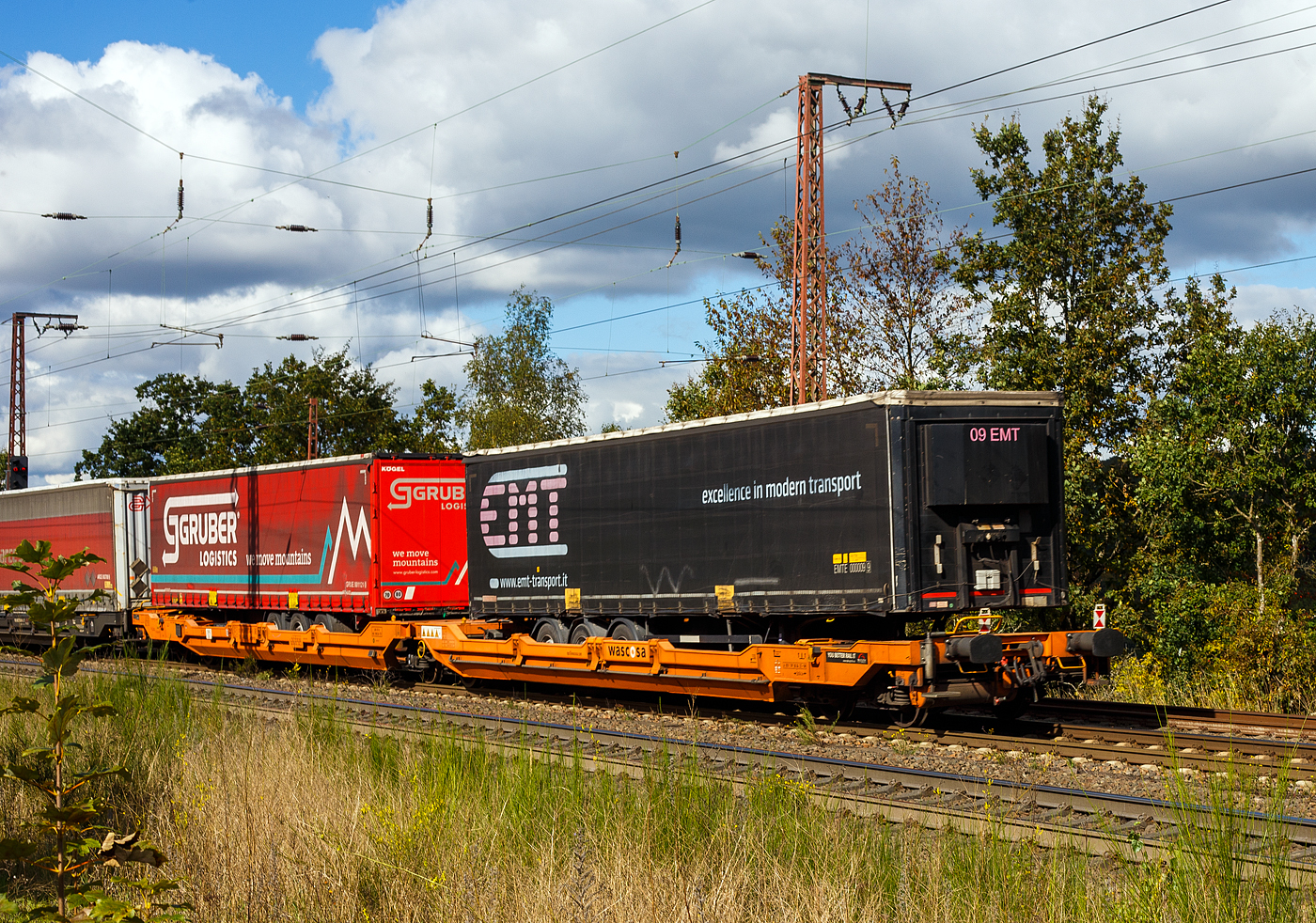 Sechsachsiger Gelenk-Taschenwagen (Doppeltaschenwagen Typ T3000e in Gelenkbauart) der Gattung Sdggmrss, 37 80 4992 358-5 D-WASCO, der WASCOSA AG (Luzern), vermietet an die TX Logistik AG (Troisdorf), am 05 Oktober 2024 im Zugverband (Zugschluss) bei der Zugdurchfahrt in Rudersdorf (Kr. Siegen). Hier beladen mit zwei Sattelanh�ngern (Trailer).
	
Der Wagen wurde von Tatravag�nka a.s. in Poprad (Slowakei) gebaut, die Entwicklung und wohl auch Lizenzgeber ist die Ferriere Cattaneo SA in Giubiasco (Schweiz). Die Fabrikschilder kann man links am Wagenende erkennen.Die Wagen vom Typ T3000e werden nach einem Patent der Cattaneo SA (Schweiz) gebaut und sind baugleich zu Wagen von Kombiverkehr, Cemat, der CFL und Wascosa. M�gliche Ladeeinheiten sind zwei Sattelauflieger oder alternativ bis zu vier Wechselbr�cken und/oder Container. Daf�r besitzt der Wagen einen dreifach verstellbaren St�tzbock sowie f�r die Ladungseinheiten feste und klappbare Aufsetzzapfen auf den Langtr�gern. Das maximale Zuladegewicht betr�gt f�r Sattelauflieger 2 � 40 t; die Basish�he liegt bei 270 mm �ber SO.

TECHNISCHE DATEN:
Spurweite: 1.435 mm (Normalspur)
L�nge �ber Puffer: 34.200 mm
Drehzapfenabstand: 2 x 14.200 mm
Radsatzstand in den Drehgestellen: 1.800 mm
Eigengewicht: 35.300 kg
Max. Zuladung bei Lastgrenze S: 100,0 t (ab Streckenklasse D)
Max. Zuladung bei Lastgrenze SS: 85,0 t (ab Streckenklasse C)
H�chstgeschwindigkeit: 100 km/h Lastgrenze S / 120 km/h bei Lastgrenze SS und leer)
Ladel�nge: 2 x 16.185 mm
Ladeh�he (f�r Container): 1.155 m
Nutzbare L�nge des Raums zwischen den Schutztr�ger: 10.490 mm
Raumbreite zwischen L�ngstr�gern: min. 2.700 mm
Kleinster befahrbarer Gleisbogen: R = 75 m
Drehgestelle: 1x Y25Ls(s)i1f und 2 x Y25Lssi1-K
Bremse: 2 x DK-GP-A (K), max. 108 t
Bremssohle: Jurid 816 M
Handbremse: Ja, auf das mittlere Drehgestell
Intern. Verwendungsf�higkeit: TEN GE / G1
