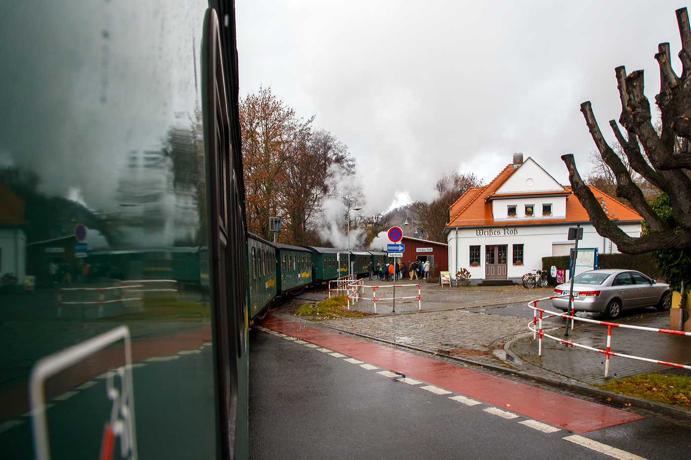 Unterwegs mit dem „Lößnitzdackel“  bzw. mit der Lößnitzgrundbahn der SDG - Sächsische Dampfeisenbahngesellschaft mbH, erreicht unser Dampfzug, gezogen von der sächsischen VII K (Altbau) 99 1761-6, nun am 07.12.2022 den Haltepunkt Weißes Roß (bei km 1,6), wir im letzten Wagen befinden uns noch am Bahnübergang Bü 1,5 - Meißner Straße in Radebeul.

Die Schmalspurbahn Radebeul Ost - Moritzburg - Radeburg ist eine sächsische Schmalspurbahn in der Spurweite von 750 mm außerhalb der sächsischen Landeshauptstadt Dresden. Für die Strecke wird heute auch die 1998 vergebene Marketingbezeichnung Lößnitzgrundbahn verwendet. Umgangssprachlich wird sie dagegen meist als Lößnitzdackel (kurz auch Dackel) oder früher Grundwurm bezeichnet.

Die in den Jahren 1911/1913 errichtete und heute denkmalgeschützte Bahnstation „Weißes Roß“ liegt nahe der Meißner Straße, wo sich die Schmalspurbahn Radebeul–Radeburg (Lößnitzgrundbahn – KBS 509) mit der Dresdner Straßenbahnlinie 4 kreuzt.

Die „Station“ besteht aus einem massiven, verputzten Bahnwärterhaus mit Fahrkartenschalter und Warteraum sowie einer nahebei gelegenen hölzernen Wartehalle. Das Bahnwärterhaus wurde 1913 durch die Königlich Sächsische Staatseisenbahnverwaltung errichtet. Es ist ein eingeschossiger, massiver Putzbau auf einem Bruchsteinsockel mit einem niedrigen Anbau, das Walmdach ist mit Ziegeln gedeckt, darin zwei Dachausbauten mit hohem Dreiecksgiebel. Die Wartehalle ist ein halboffenes, verbrettertes Fachwerk mit Pultdach.