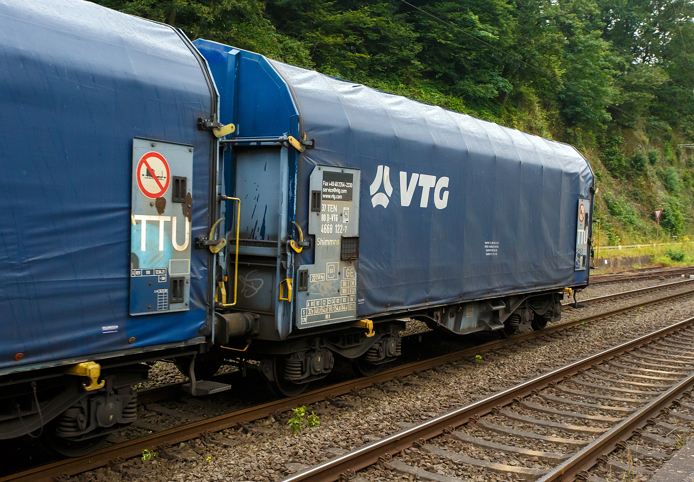 Vierachsiger Drehgestell-Flachwagen mit verschiebbarem Planenverdeck und Lademulden für Coiltransporte, 37 80 4668 122-7 D-VTG, der Gattung Shimmns-ttu (VTG Bez. F46.520D), der VTG Rail Europe GmbH (Hamburg), am 03 Juli 2024 eigereiht im Zugverband (Zudschluss) der KSW bei einer in Zugdurchfahrt im Bf Scheuerfeld/Sieg, in Richtung Herdorf via Betzdorf.

Diese Wagen sind speziell für den Transport witterungsempfindlicher Blechrollen (Coils) bestimmt. Er besitzt feste Stirnwände, 5 fest im Untergestell eingebaute Lademulden. Die Wagenabdeckung erfolgt mit einer PVC-beschichteten Gewebeplane, die auf 11 Rohrrahmen aufliegt. Über Laufwagen ist das Planendach in Wagenlängsrichtung verschiebbar. Die Verriegelung des Planendaches an den Stirnwänden erfolgt über eine 4-Punkt-Zentralverriegelung, die sowohl vom Erdboden als auch von der Rampe aus bedient werden kann. Das Planenverdeck lässt sich an einem Wagenende so weit zusammenschieben, dass ca. 2/3 der Ladefläche zur Beladung freigegeben wird. Hierdurch ist eine einfache Beladung des Wagens sowohl von oben als auch von der Seite aus möglich.

TECHNISCHE DATEN:
Spurweite: 1.435 mm
Achsanzahl: 4 (in 2 Drehgestelle)
Länge über Puffer: 12.040 mm
Länge der Ladefläche: 10.800 mm
Drehzapfenabstand: 7.000 mm
Achsabstand im Drehgestell: 1.800 mm
Eigengewicht: 22.250 kg
Höchstgeschwindigkeit: 100 km/h (beladen) / 120 km/h (leer)
Maximales Ladegewicht: 67,7 t (ab Streckenklasse D4), DB CM 61,7 t
Mulden: 5 Stück, im Untergestell integriert
Werkstoff Muldenmatten: Tecthan
Festlegearme: 20 Stück, stufenlos verstellbar, ausgestattet mit Schutzplatten
Coil-Breite: min. 342 mm bis max.  2.042 mm
Kleinster bef. Gleisbogenradius: 35 m
Bauart der Bremse: KE-GP-A (K)
Bremssohle: C 810
Intern. Verwendungsfähigkeit: TEN-GE