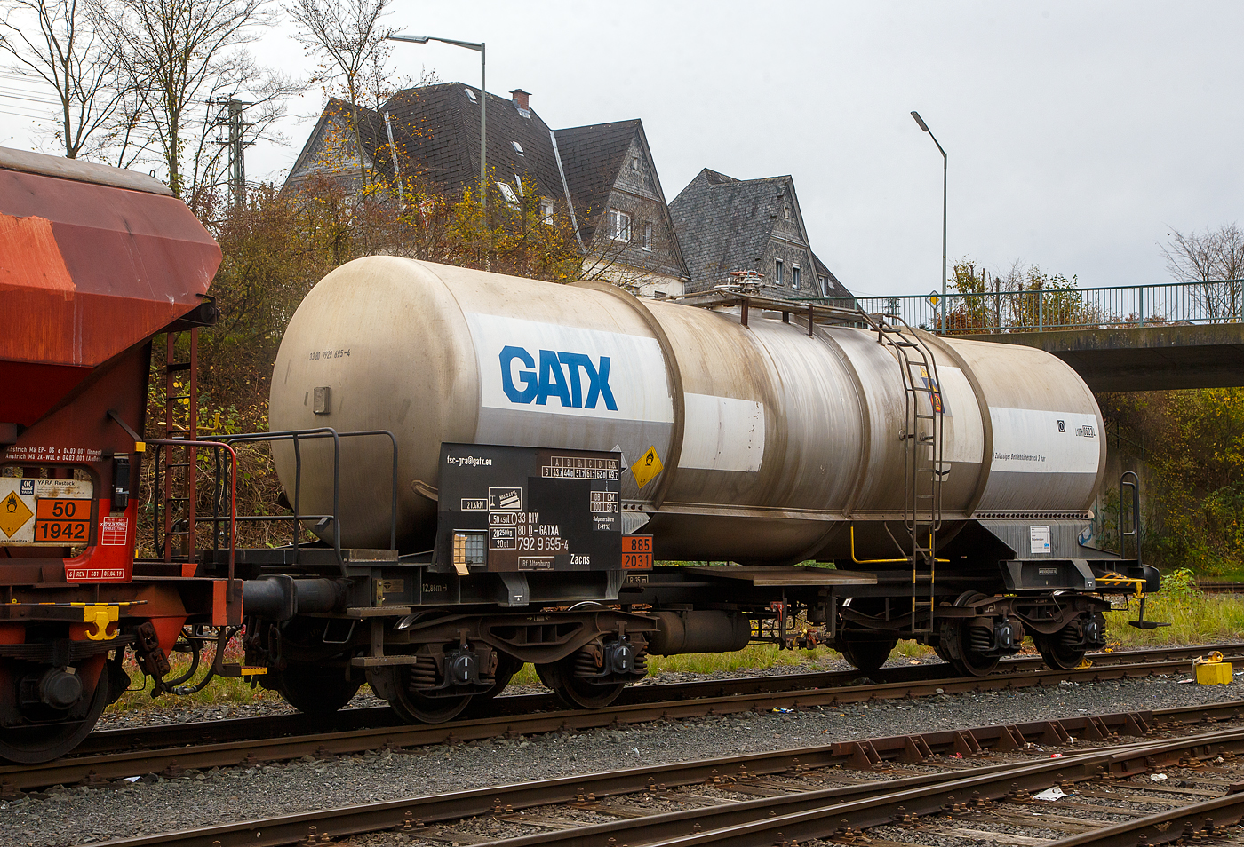 Vierachsiger-Drehgestell Kesselwagen für Salpetersäure (>97%) mit Bremserbühne, der Gattung Zacns, registriert als 33 80 7929 695-4 D-GATXD der GATX Rail Germany GmbH abgestellt, im Zugverband eines Übergabezuges der KSW, am 03.11.2022 in Herdorf auf dem Rbf. der KSW. Mieter des Wagens ist die SKW Stickstoffwerke Piesteritz GmbH (Wittenberg). 

Die Gefahrguttafel (885/2031) zeigt es auch noch an: (oben) Gefahrgutnummer 885 = stark ätzender Stoff / (unten) UN-Nummer 2031 = Salpetersäure, andere als rotrauchend, mit mehr als 70 % Säurebrandfördernd. Hier sogar (laut Anschrift) größer 97 %. Die reine Säure ist farblos und hat einen scharf stechenden Geruch. Sie wird unteranderem zur Herstellung von Sprengstoffen verwendet, was hier der Fall ist.

Der Wagen wurde 2003 vom rumänischen Wagonbauer Meva S.A. DrobetaTurnu – Severin gebaut,

TECHNISCHE DATEN:
Gattung: Zacns (Gattungszahl 7629)
Spurweite: 1.435 mm
Länge über Puffer : 12.860 mm
Drehzapfenabstand: 7.820 mm
Achsabstand im Drehgestell: 1.800 mm
Laufraddurchmesser 920 mm (neu)
Höchstgeschwindigkeit: 100 km/h
Eigengewicht: 20.250 kg
Nutzlast: 69,7 t ab Streckenklasse D3 (CM 63,7 t)
Kleinster befahrbarer Gleisbogen: R 35 m
Gesamtvolumen: 50,450 Liter
Prüfdruck: 4 bar
Zulässiger Betriebsüberdruck: 3 bar
Tankcode: L10DH
Behälterwerkstoff : Edelstahl
Intern. Verwendungsfähigkeit: RIV

Auch im dahinter befindlichen Wagen dem gedeckten Schüttgutwagen 21 80 0734 600-8 D-DB, der Gattung Tds 937, wurde ein Rohstoff für die Herstellung von Sprengstoffen transportiert und zwar Ammoniumnitrat.