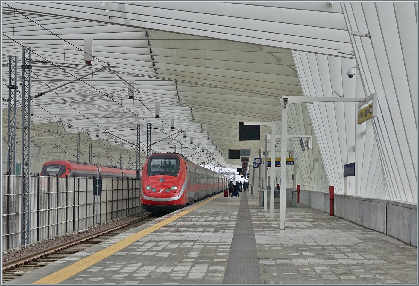 Während ein FS Trenitalia ETR 500 in der wunderschönen Halle des Bahnhofs von Reggio Emilia AV auf der Fahrt nach Norden kurz anhält; fährt kaum zu sehen links im Bild der bereits bei der Einfahrt gezeigte ETR 400 044 mit einem sehr hohen Tempo durch den Bahnhof. 
Der Bahnhof wurde durch den Architekten Santiago Calatrava geplant.

14. März 2023