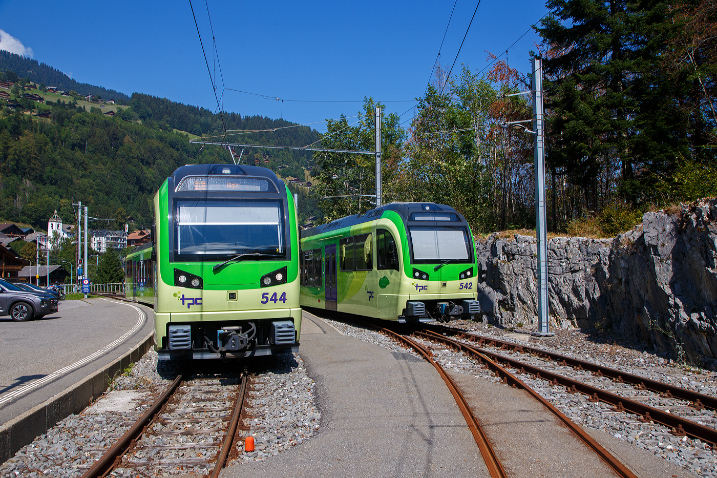 Zwei tpc AOMC/ACD Beh 2/6 meterspurige Triebzüge mit gemischtem Adhäsions- und Zahnradbetrieb vom Typ Stadler SURF stehen am 08 September 2023 im Endbahnhof der AOMC in Champéry (1.037 m ü. M.). Links der Triebzug 544 und rechts 542. SURF steht für Série Unifiée Romande pour Réseau Ferré métrique (Einheitliche Serie für das Westschweizer Meterspurige Schienennetz).

Die AOMC (Chemin de fer Aigle–Ollon–Monthey–Champéry, deutsch Aigle-Ollon-Monthey-Champéry-Bahn, war eine Eisenbahngesellschaft in den Schweizer Kantonen Waadt und Wallis. Sie entstand 1946 aus der Fusion der 1907 eröffneten Chemin de fer électrique Aigle–Ollon–Monthey (AOM) mit der 1909 eröffneten Chemin de fer Monthey–Champéry–Morgins (MCM) und fusionierte 1999 zu den Transports Publics du Chablais (TPC).

Die 23,4 Kilometer lange Strecke der verbindet Aigle durch das Rhonetal mit Monthey (reine Adhäsionsbahn) und führt anschließend als Bahn mit gemischtem Adhäsions- und Zahnradbetrieb nach Champéry im Val d’Illiez. Oben direkt neben dem Endbahnhof Champéry befindet sich die Talstation der Luftseilbahn Champéry-Croix de Culet (Planachaux). 

Im Sommer 2016 wurde die Strecke umfassend modernisiert. Dabei wurden die Zahnstangenabschnitte vollständig erneuert und das bisherige Zahnstangensystem Strub durch Abt-Zahnstangen ersetzt. Weiter wurde die Fahrleitungsspannung von 950 auf 1500 V erhöht. Somit besitzen alle ab Aigle verkehrenden Strecken der TPC das gleiche Zahnstangensystem und die gleiche Spannung. Der Verkehr wird nun vollständig mit den neu abgelieferten Beh 2/6 541–547 abgewickelt. Von den bestehenden Triebfahrzeugen der AOMC wurden einzig die beiden im Jahr 2001 gelieferten Doppeltriebwagen Beh 4/8 591–592 an das neue Zahnstangen- und Stromsystem angepasst.
