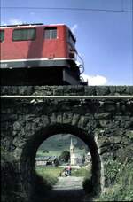 RhB Ge 6/6 II in Bergün, im Hintegrund, durch den Bogen des Durchgangs ist die Kirche von Bergün zu sehen, im August 1990.