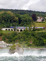 W�hrend tobend die Wassermassen den Rheinfall bei Schaffhausen herab st�rzen, f�hrt eine SBB Re 450 mit Doppelstock-Pendelz�gen am 18.06.2016, als S 9 (Uster – Z�rich HB – Schaffhausen) der S-Bahn Z�rich, �ber den Hangviadukt in Neuhausen am Rheinfall und erreicht bald die gleichnamentliche Station.